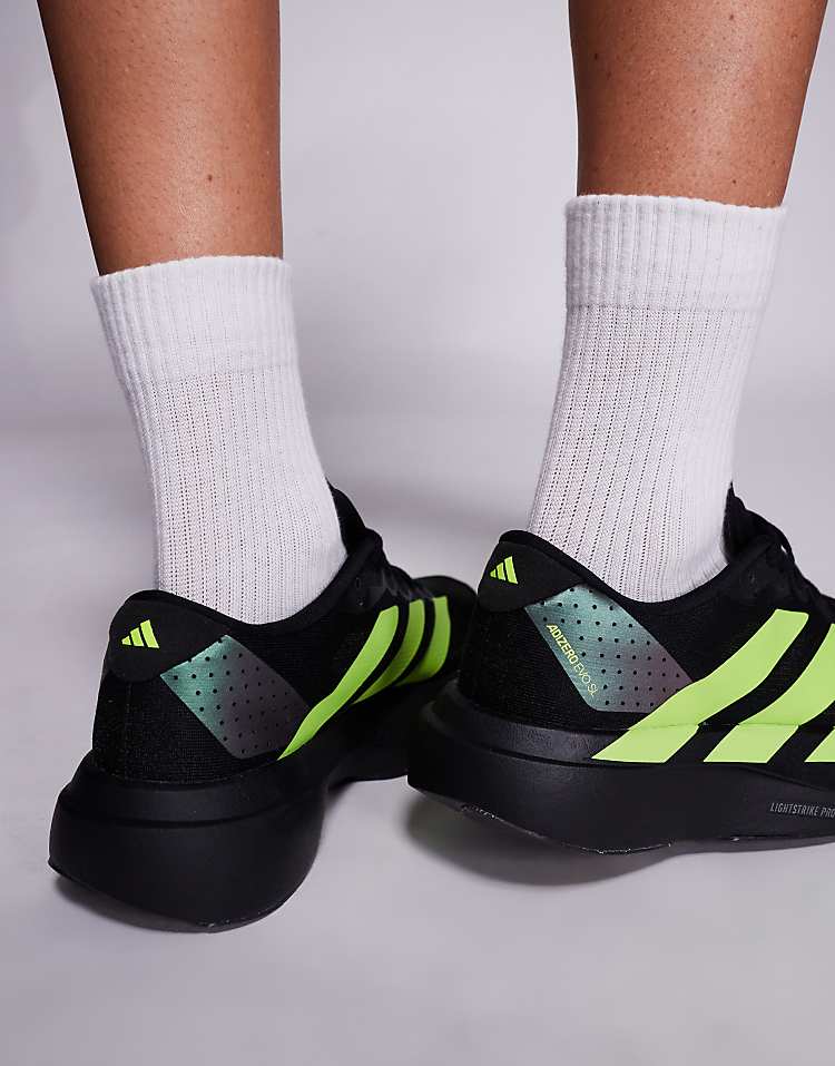 Close-up of black adidas Adizero Evo SL sneakers with neon green stripes on feet wearing white socks