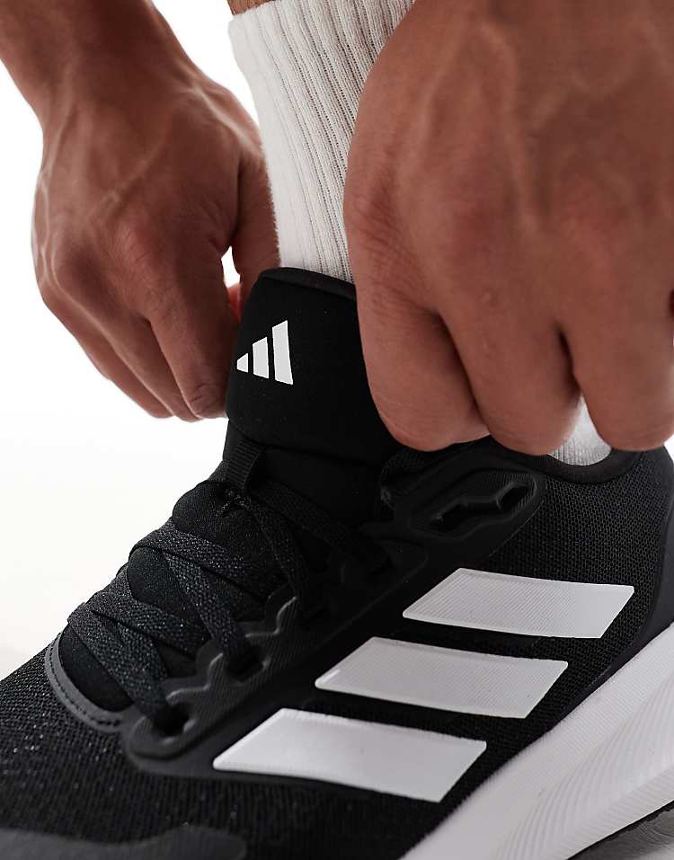Close-up of hands tying black adidas RunFalcon running shoes with white stripes on feet