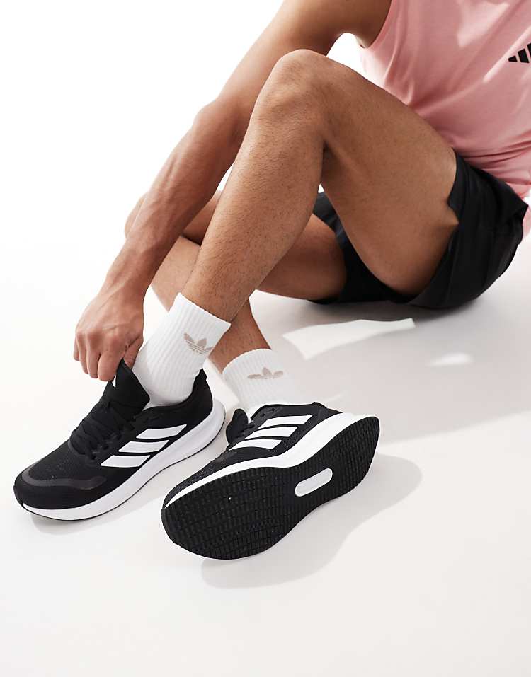 Man wearing black and white adidas RunFalcon running shoes tying laces while sitting on floor