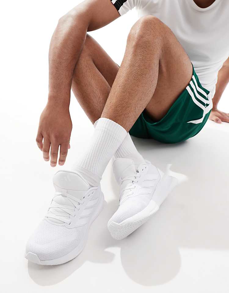 Men wearing white adidas RunFalcon running shoes with white socks sitting on floor in athletic shorts