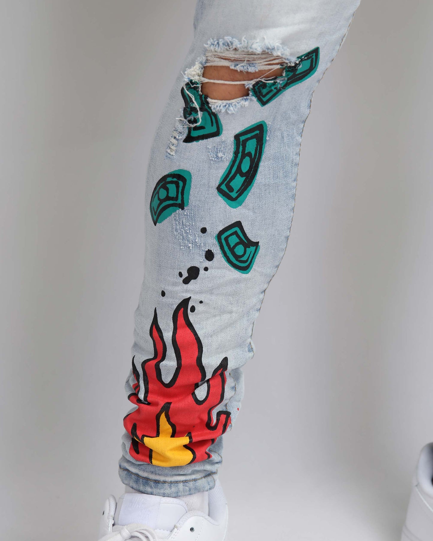 Anime style ripped jeans with colorful graphic designs of money and flames on distressed denim