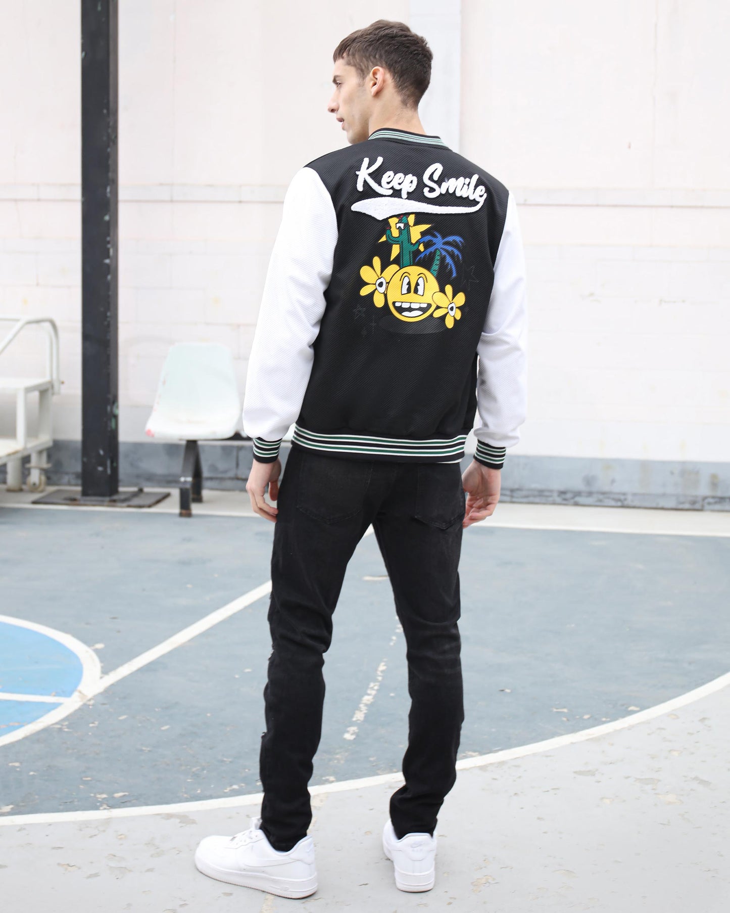 Man wearing black graffiti slim-fit jeans with a stylish varsity jacket for a trendy streetwear look