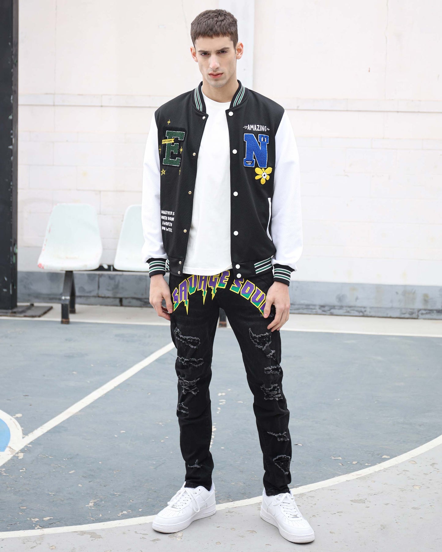 Stylish male model wearing black graffiti slim-fit jeans with a varsity jacket and white sneakers