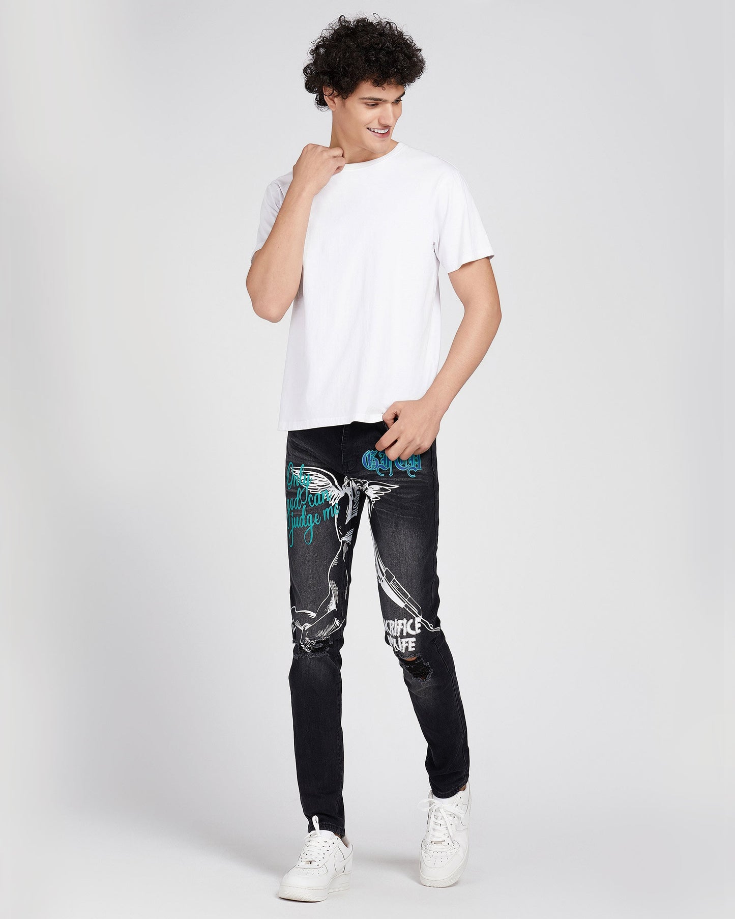 Man wearing Logeqi black ripped graffiti jeans with white graphic designs paired with a plain white t-shirt and white sneakers