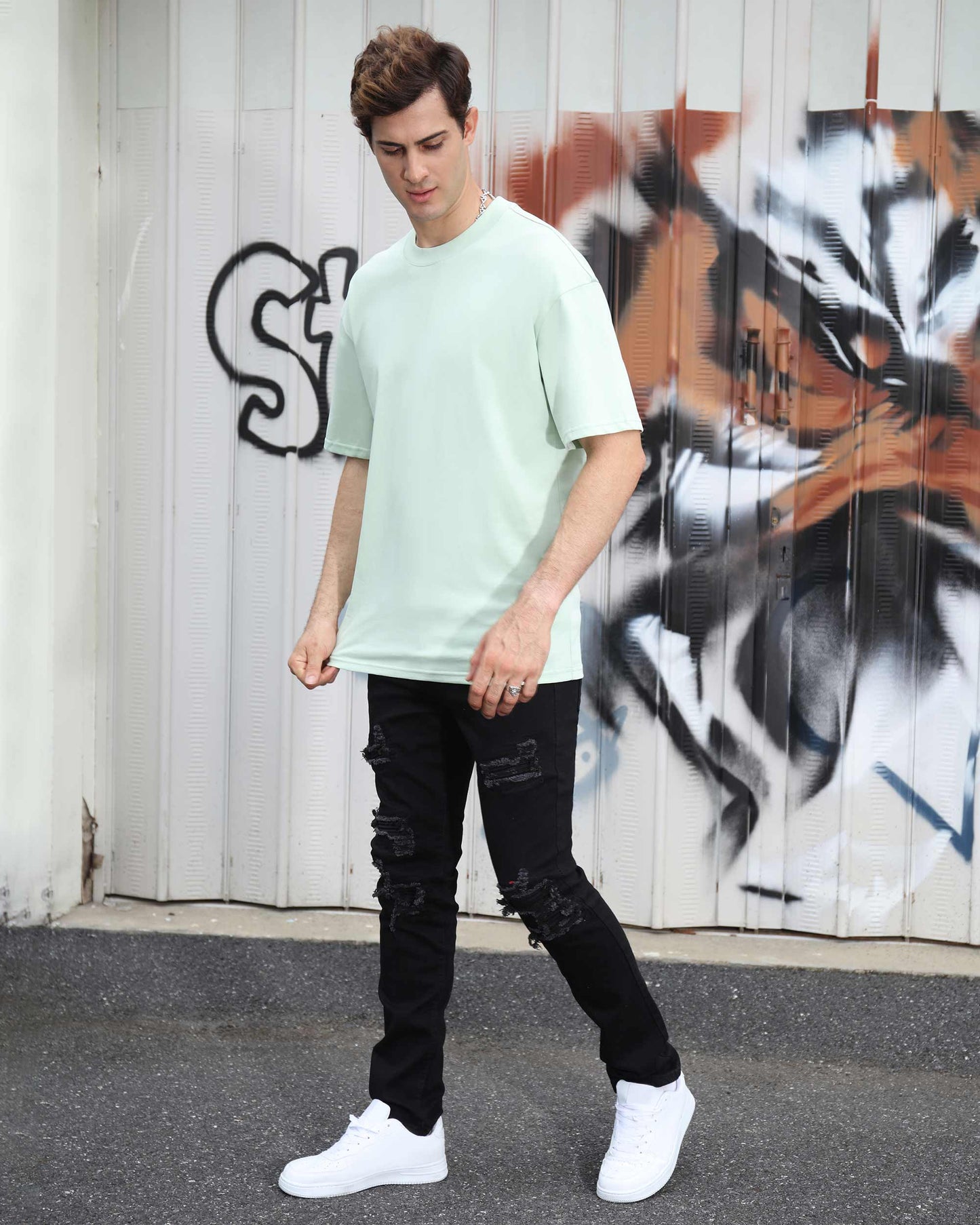 Stylish man wearing black ripped jeans for men and a light green t-shirt on city street