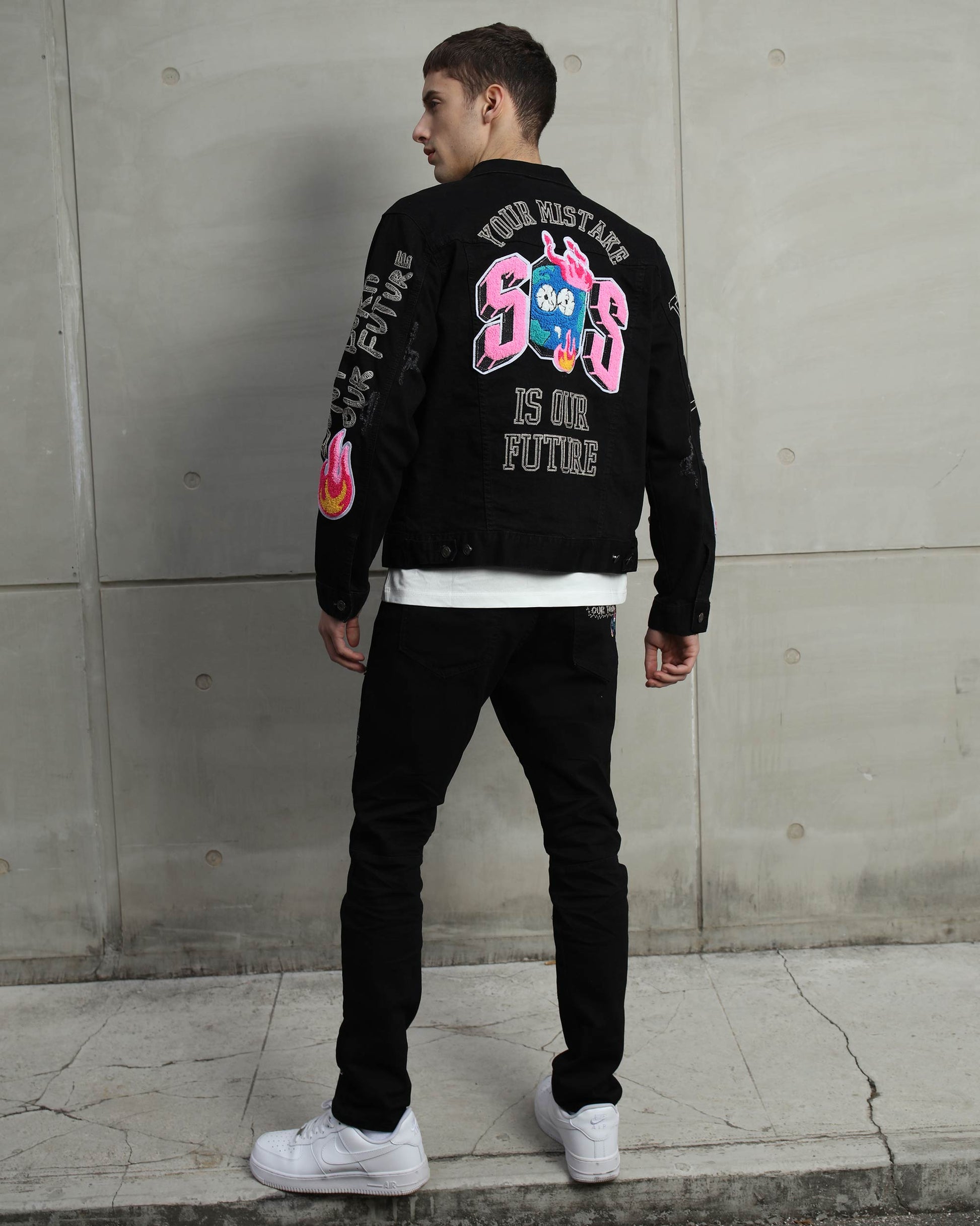Model wearing black streetwear patchwork jeans paired with a colorful graphic jacket