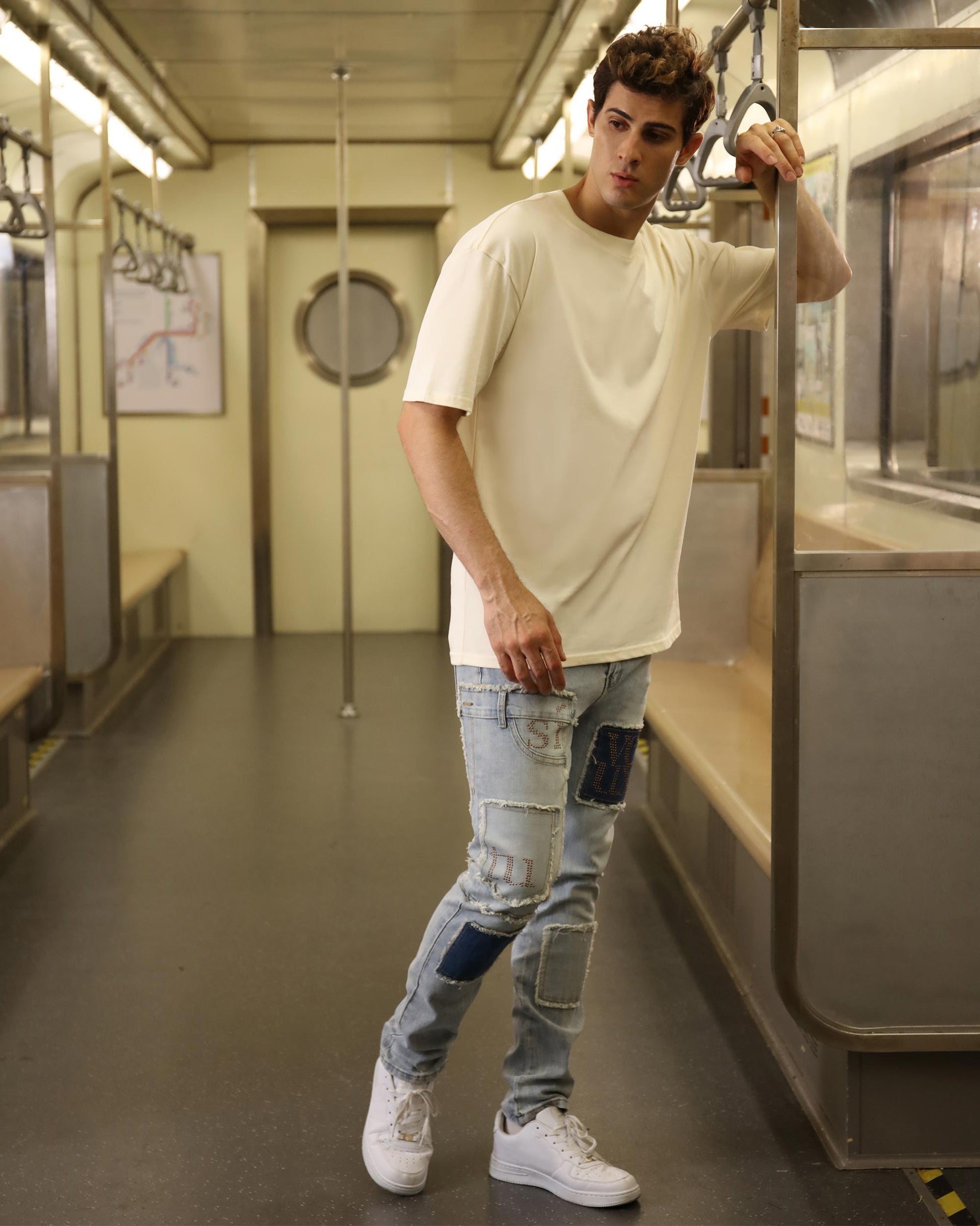 Logeqi blue jeans with diamond accents worn by a male model in a subway car with patched design