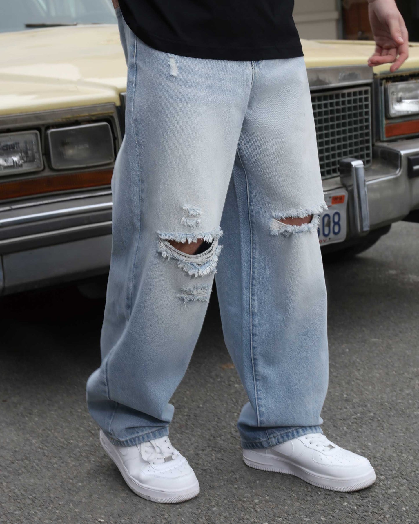 Logeqi blue ripped baggy jeans with distressed holes worn with white sneakers outdoors