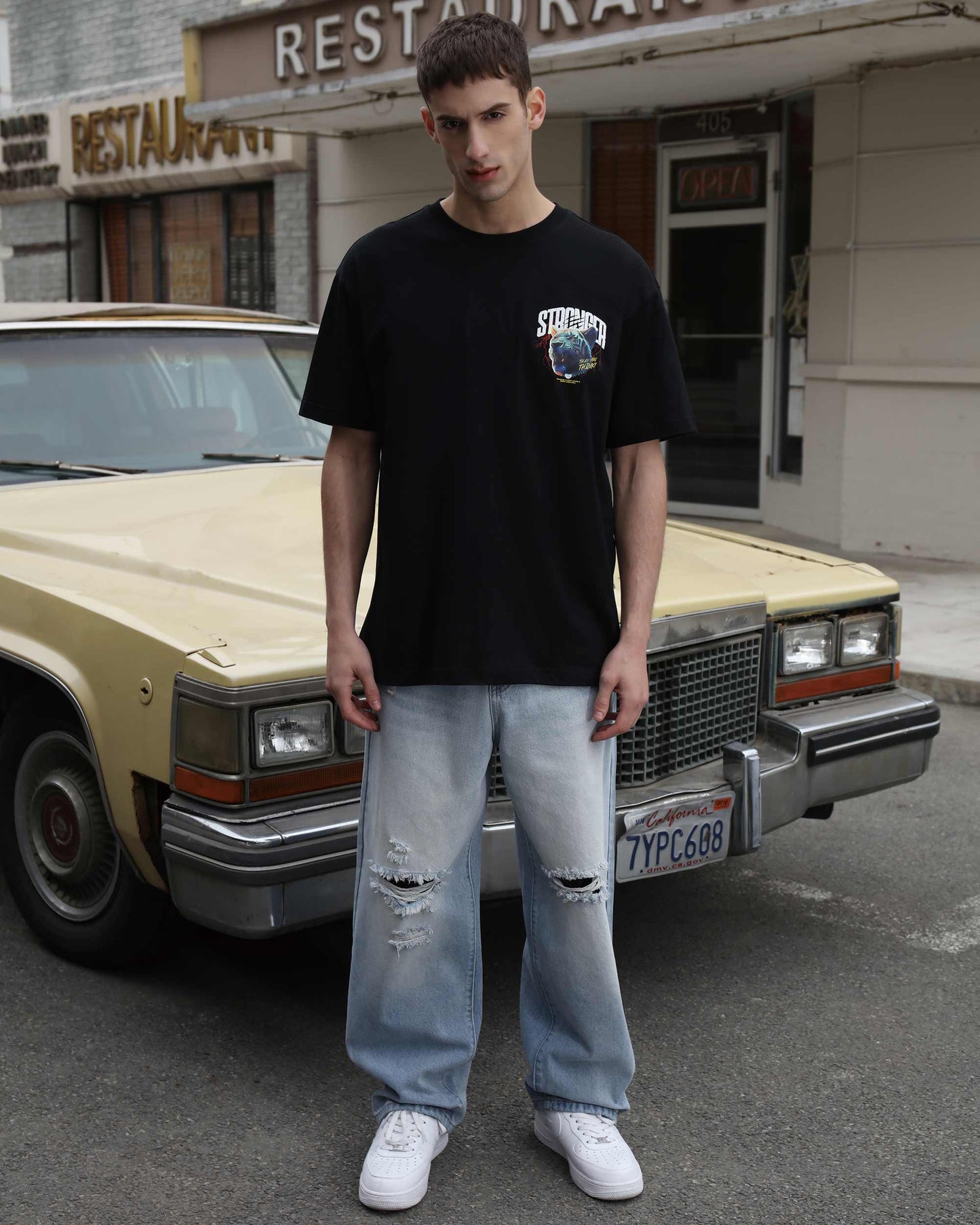 Logeqi blue ripped baggy jeans worn by male model standing in front of vintage car on street