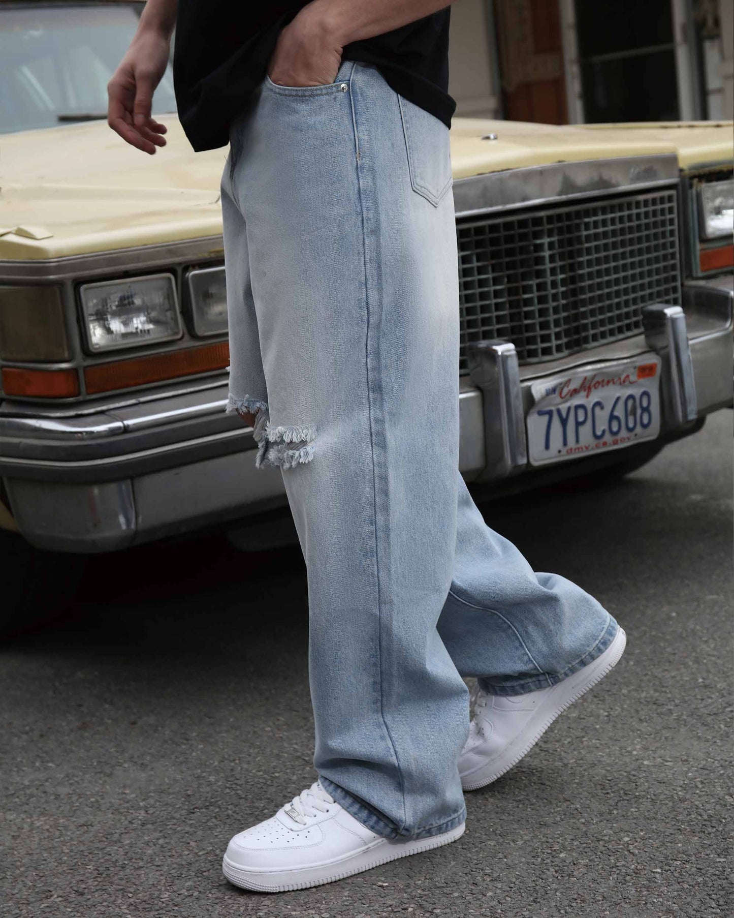 Logeqi blue ripped baggy jeans worn with white sneakers standing by vintage car