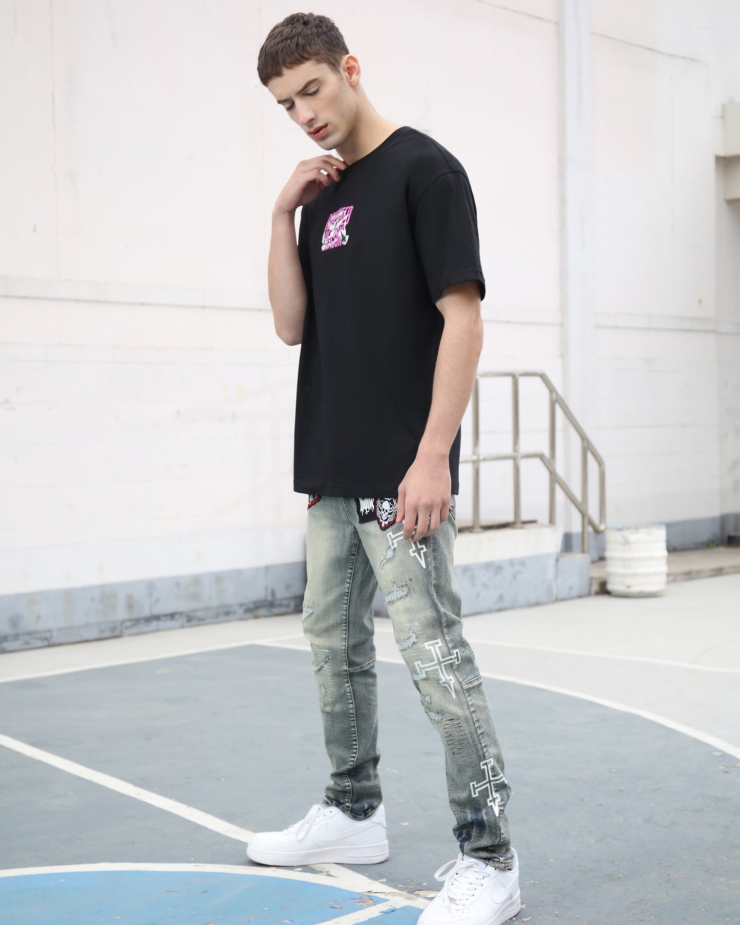Stylish model wearing blue ripped jeans with skull print paired with a black t-shirt and white sneakers