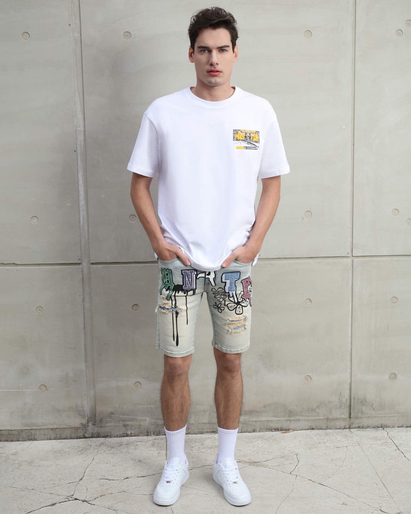 Man wearing Logeqi distressed graffiti denim shorts paired with a white graphic t-shirt and white sneakers