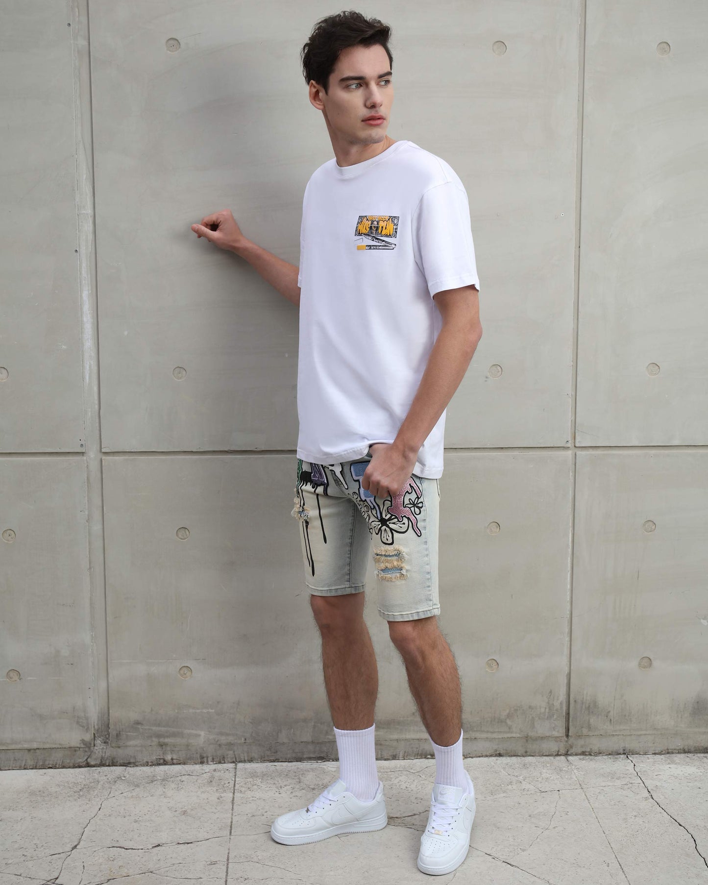 Man wearing Logeqi distressed graffiti denim shorts paired with white t-shirt and sneakers