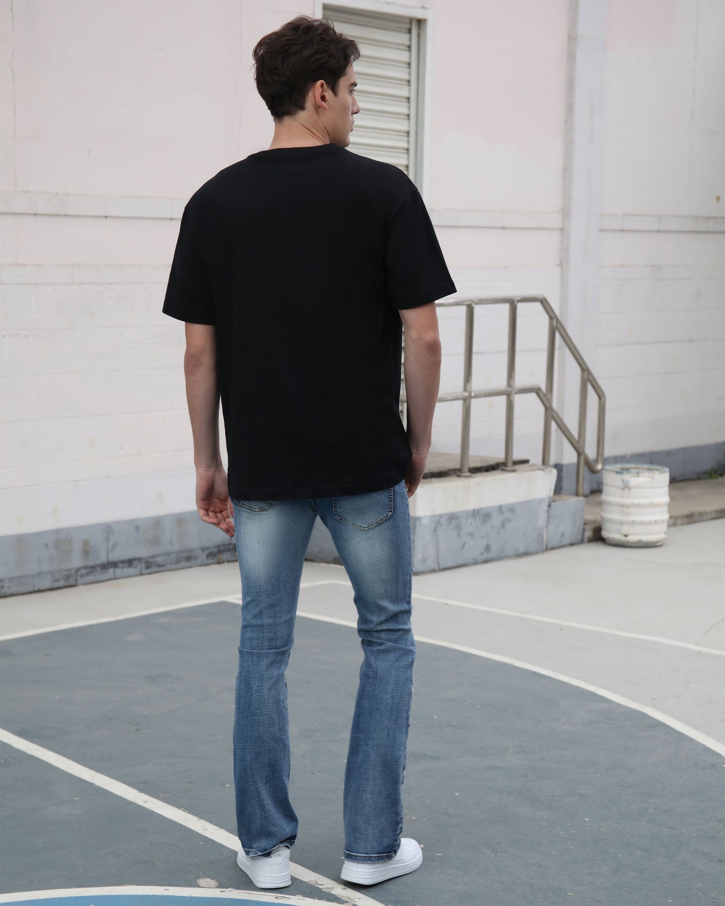 Man wearing Logeqi medium wash ripped jeans standing outdoors on a basketball court