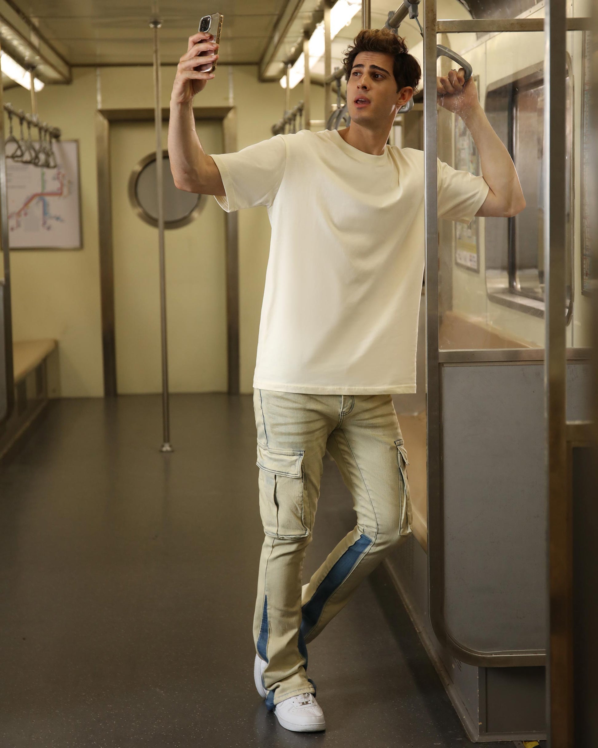 Man taking a selfie in industrial style cargo jeans inside a subway train
