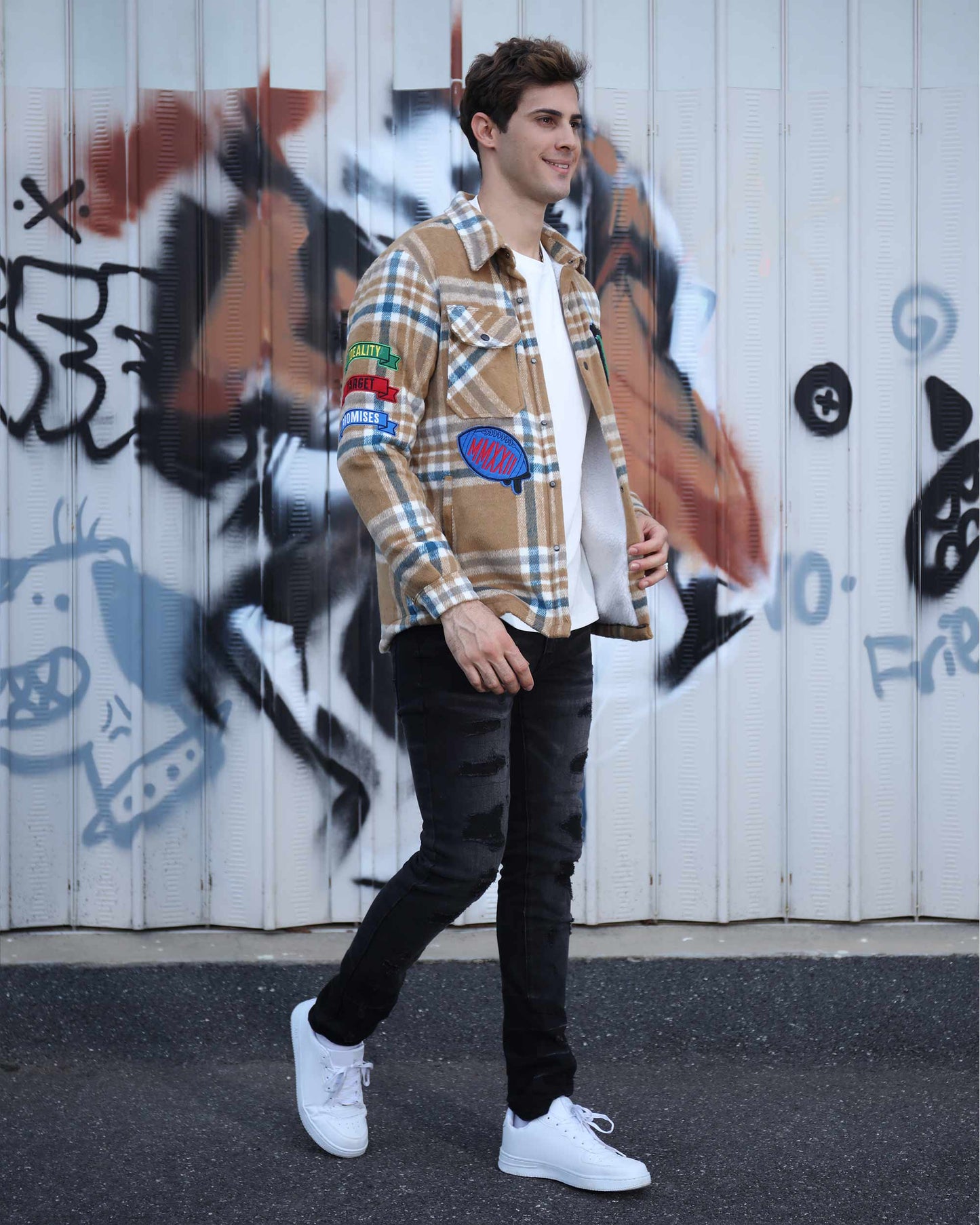 Man wearing a checkered plaid moto jacket with patches, pairing it with black jeans and white sneakers