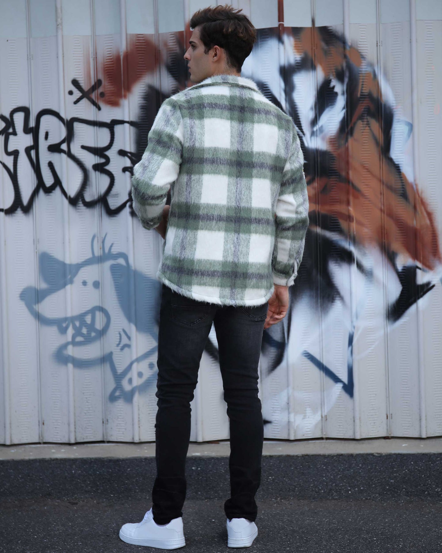 Man wearing Logeqi classic plaid moto jacket in green and white standing against graffiti wall