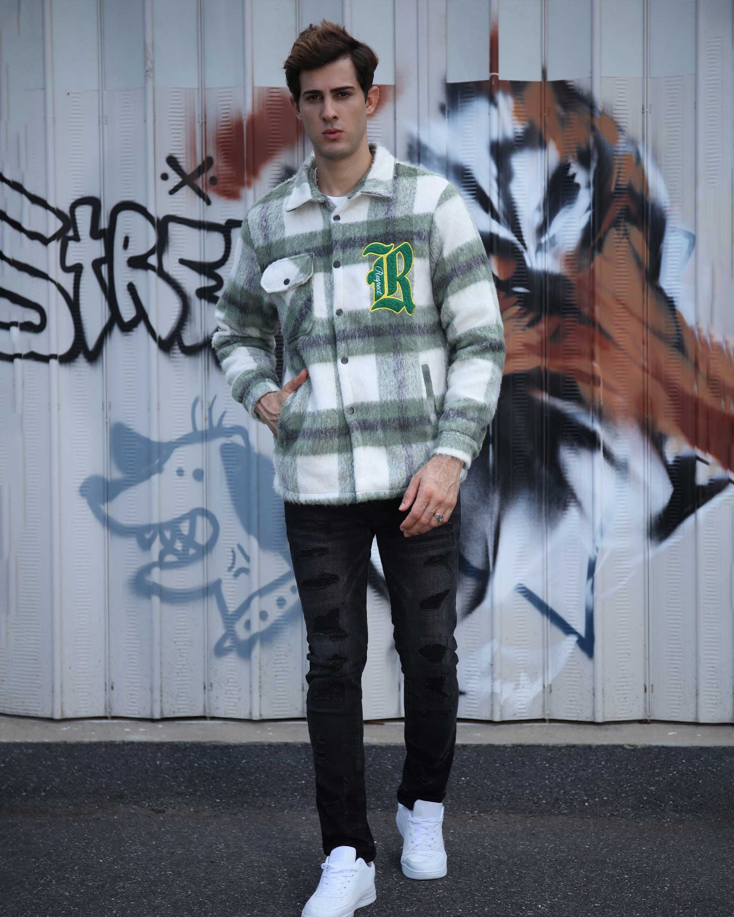 Man wearing Logeqi classic plaid moto jacket in green and white standing in front of graffiti wall