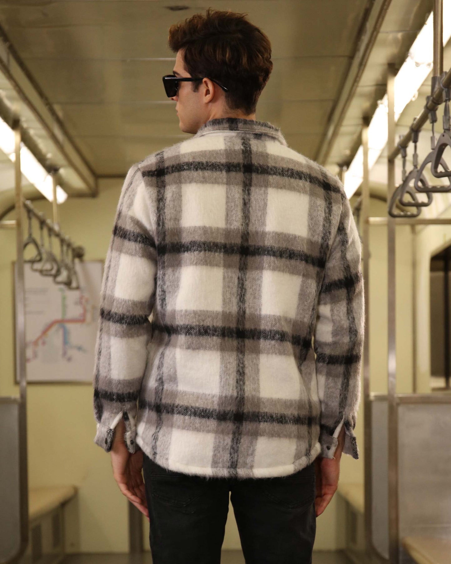 Back view of a man wearing Logeqi classic plaid moto jacket in white and gray inside a subway train