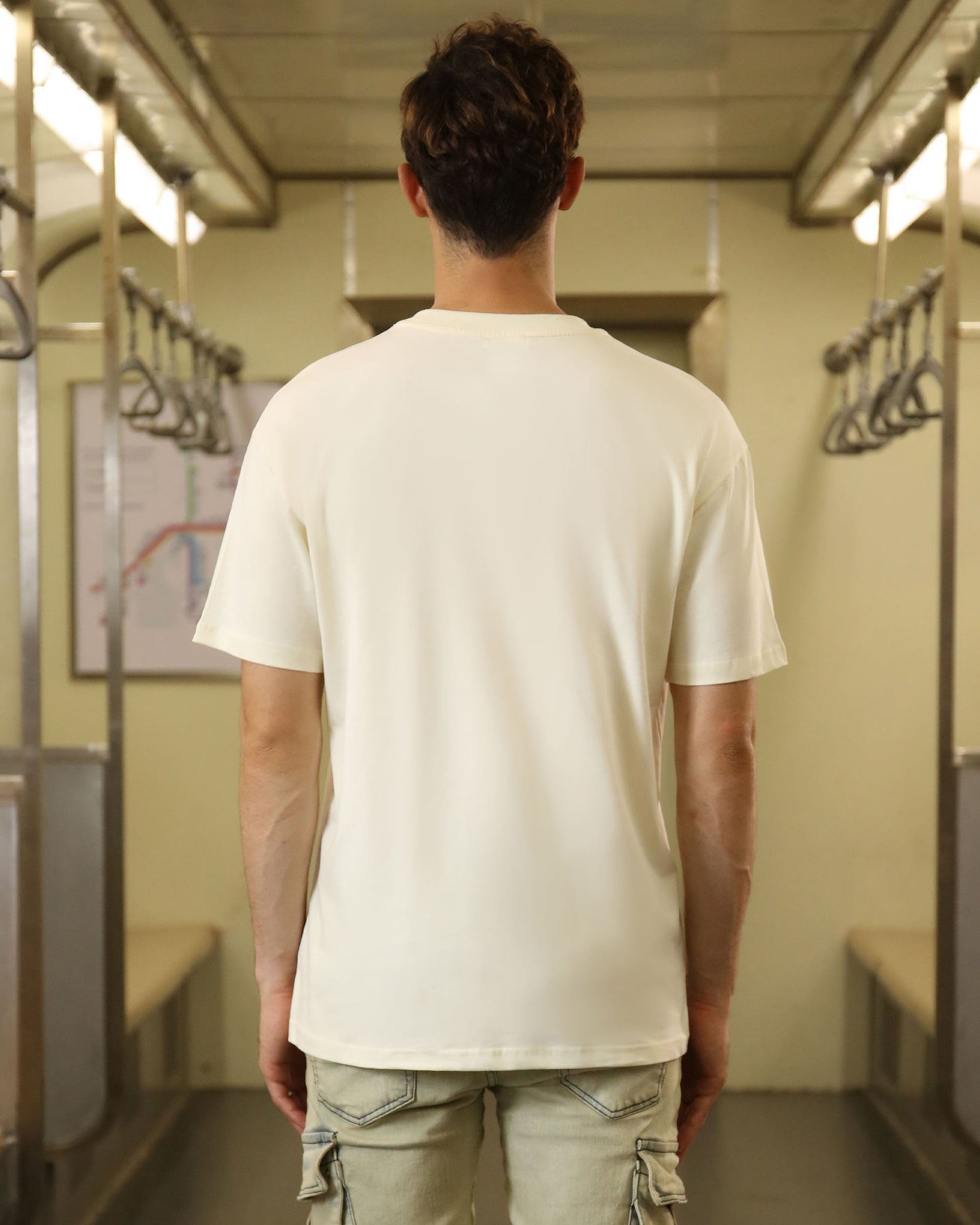 Back view of a man wearing a cream oversized t-shirt in a subway train interior