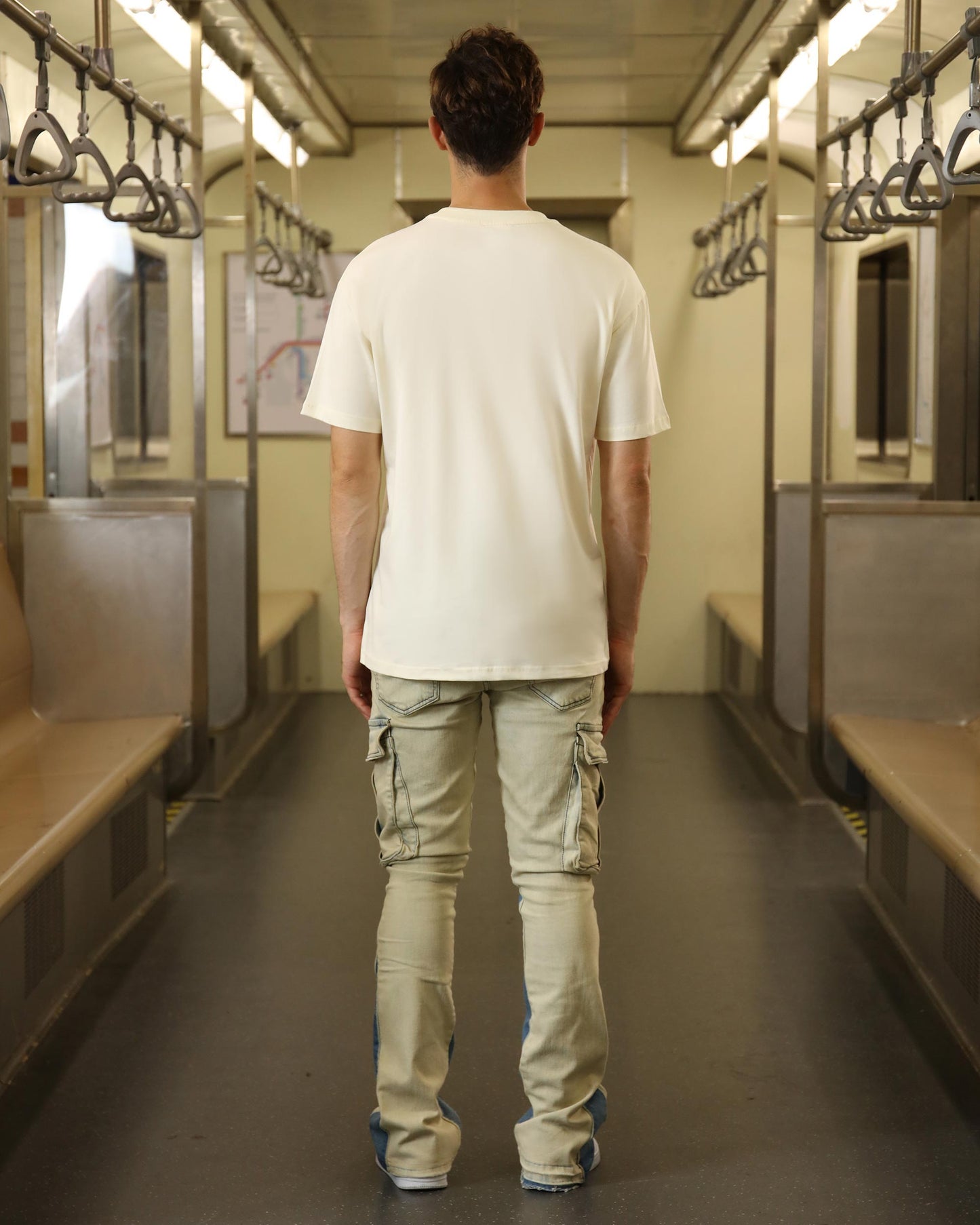 Man wearing a cream oversized t-shirt while standing in a train carriage