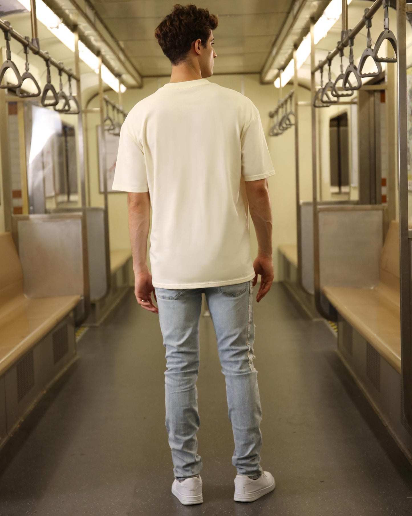 Man wearing a cream oversized t-shirt in a subway train, showcasing a comfortable casual style