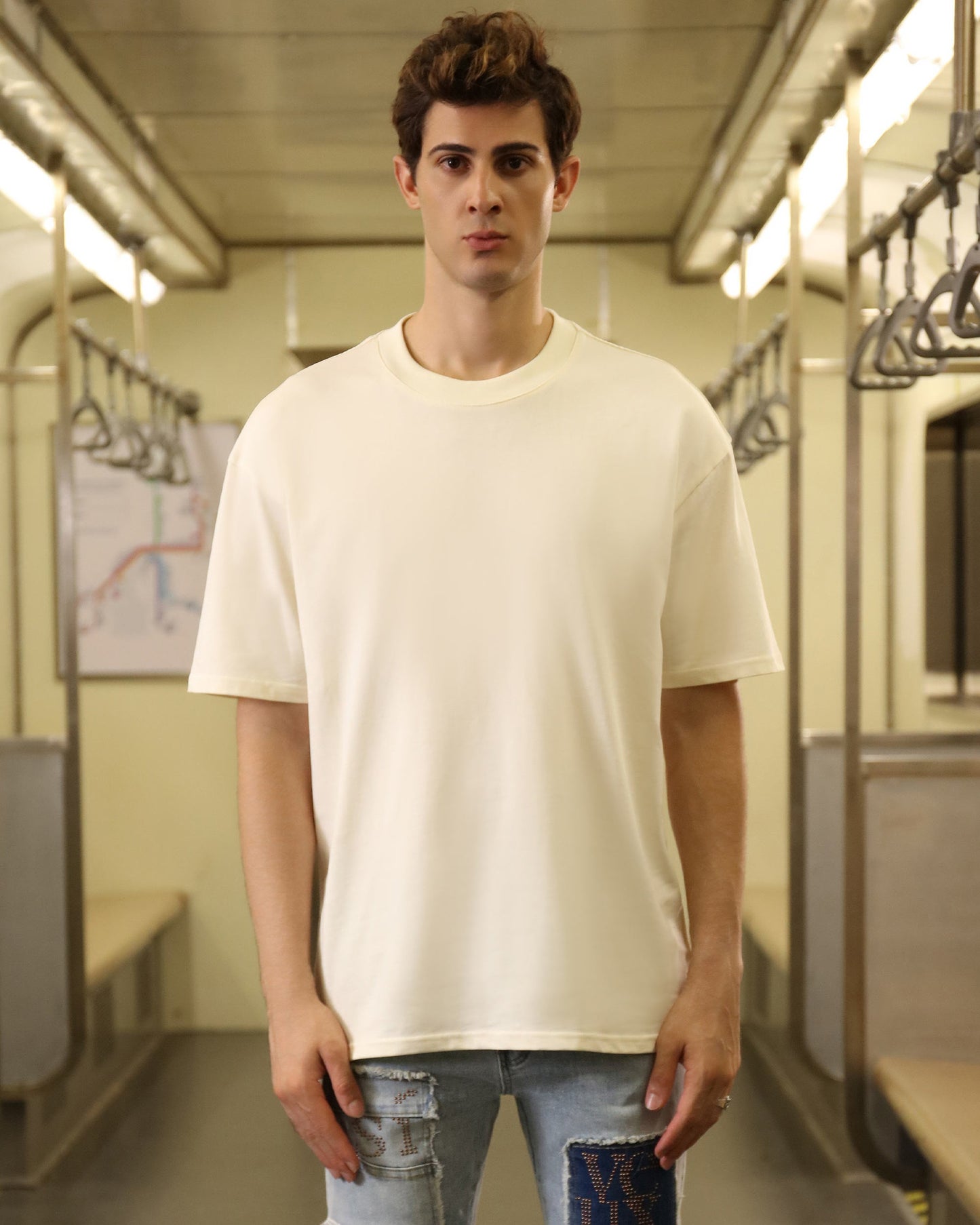Man wearing a cream oversized t-shirt in a train setting, styled for casual comfort