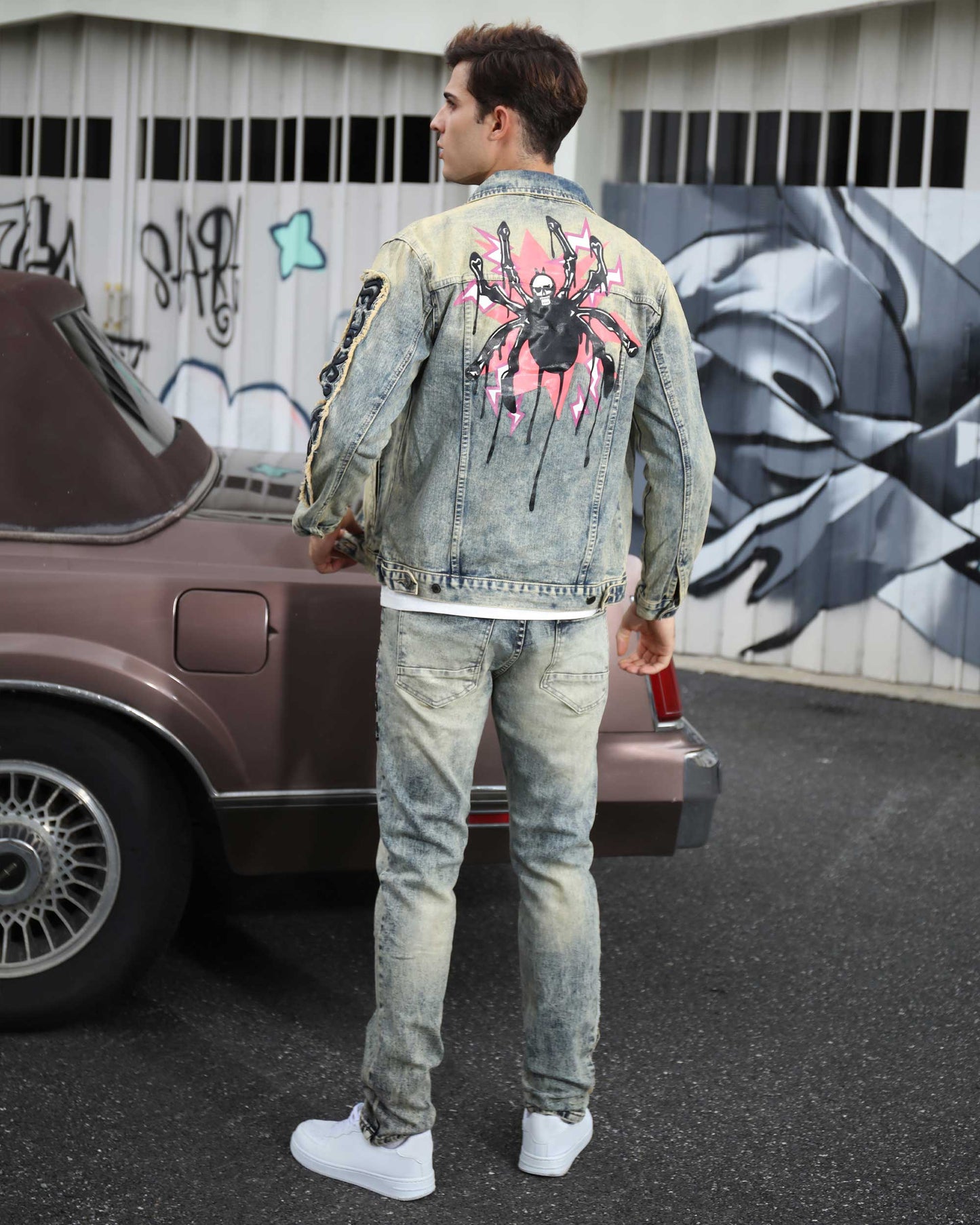 Man wearing dark washed straight leg jeans with a stylish denim jacket featuring a spider graphic