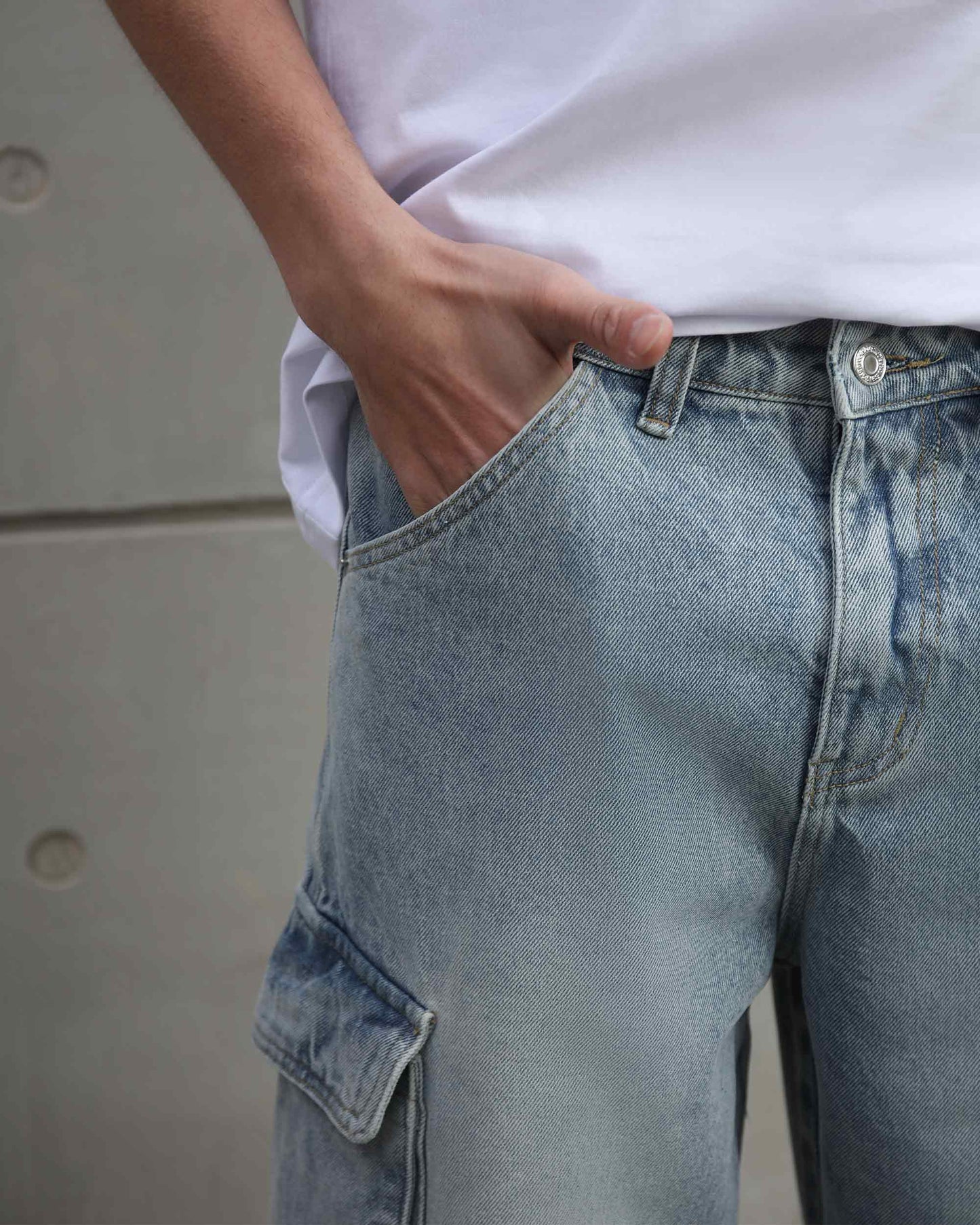 Close-up of distressed blue baggy jeans by Logeqi worn with hand in pocket and white t-shirt