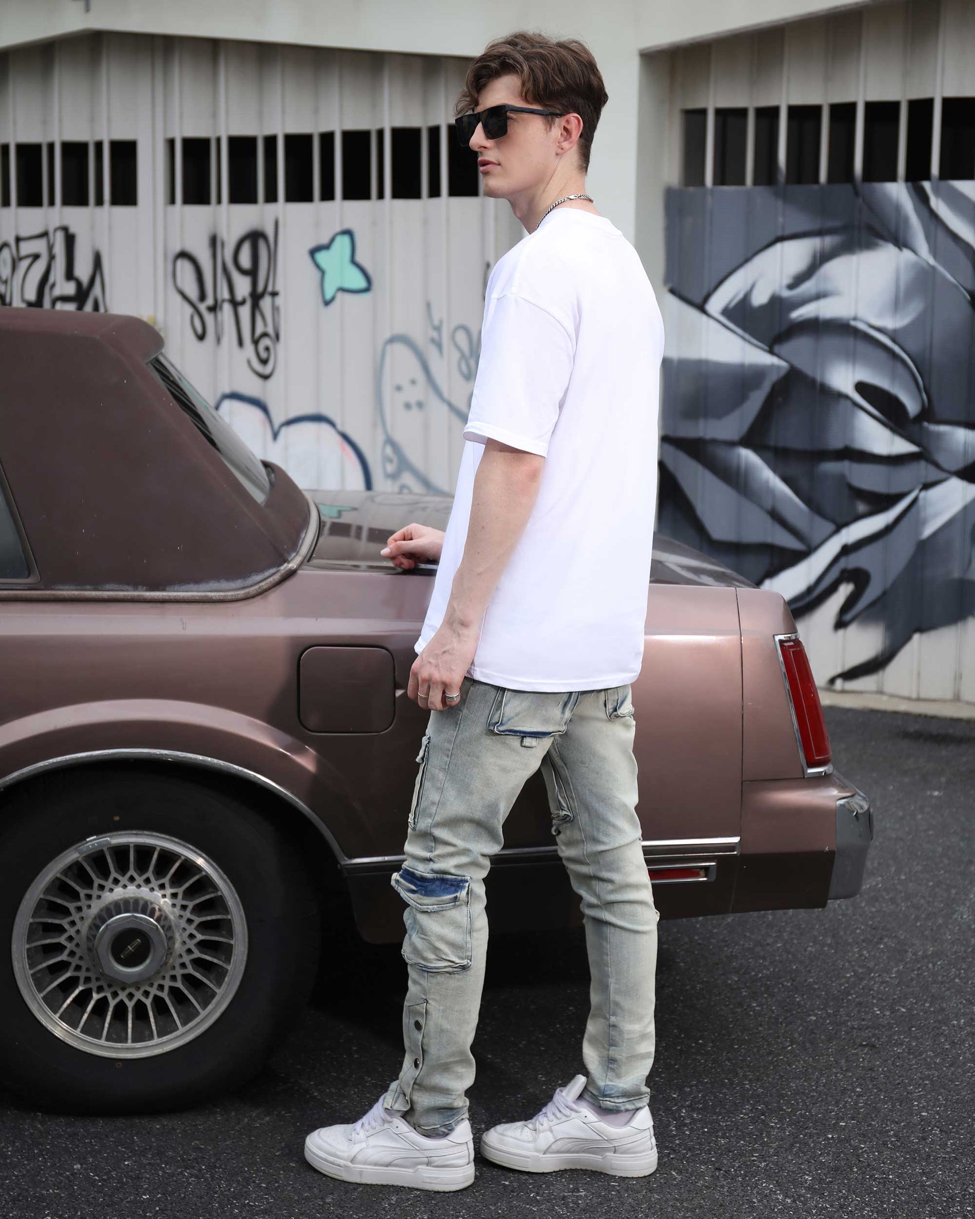 Man wearing Logeqi distressed cargo jeans men paired with white t-shirt and sunglasses standing next to vintage car