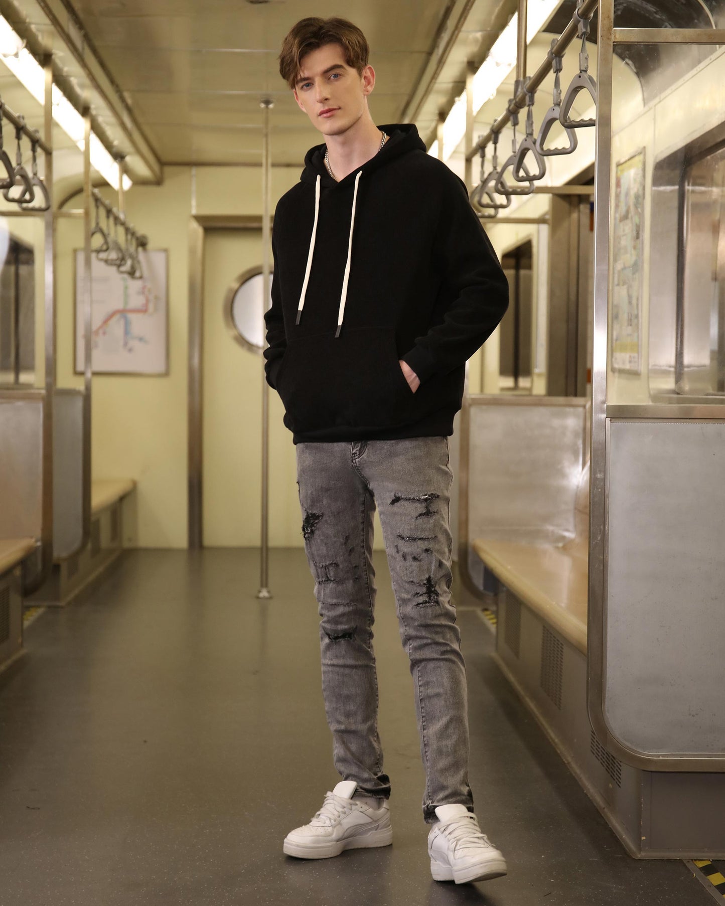 Logeqi gray ripped jeans men styled with a black hoodie and white sneakers in a subway setting