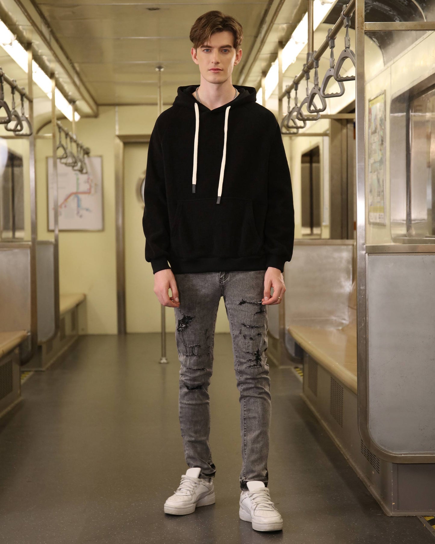 Man wearing Logeqi gray ripped jeans men styled with black hoodie and white sneakers in subway