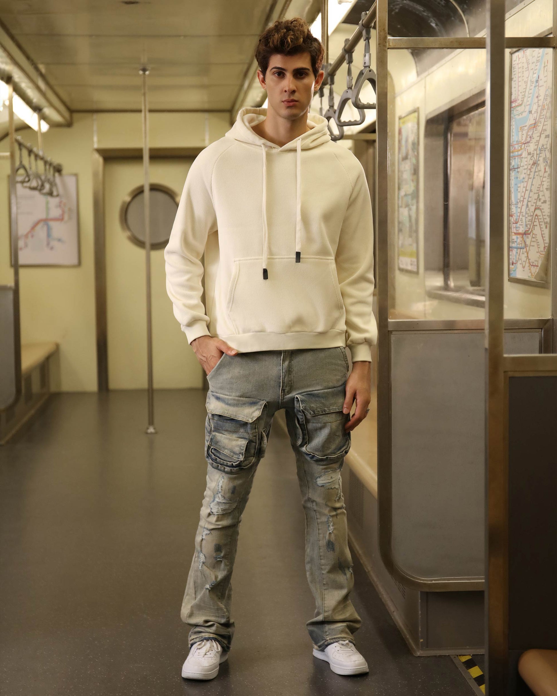 Model wearing light wash cargo jeans with a cream hoodie in a subway setting