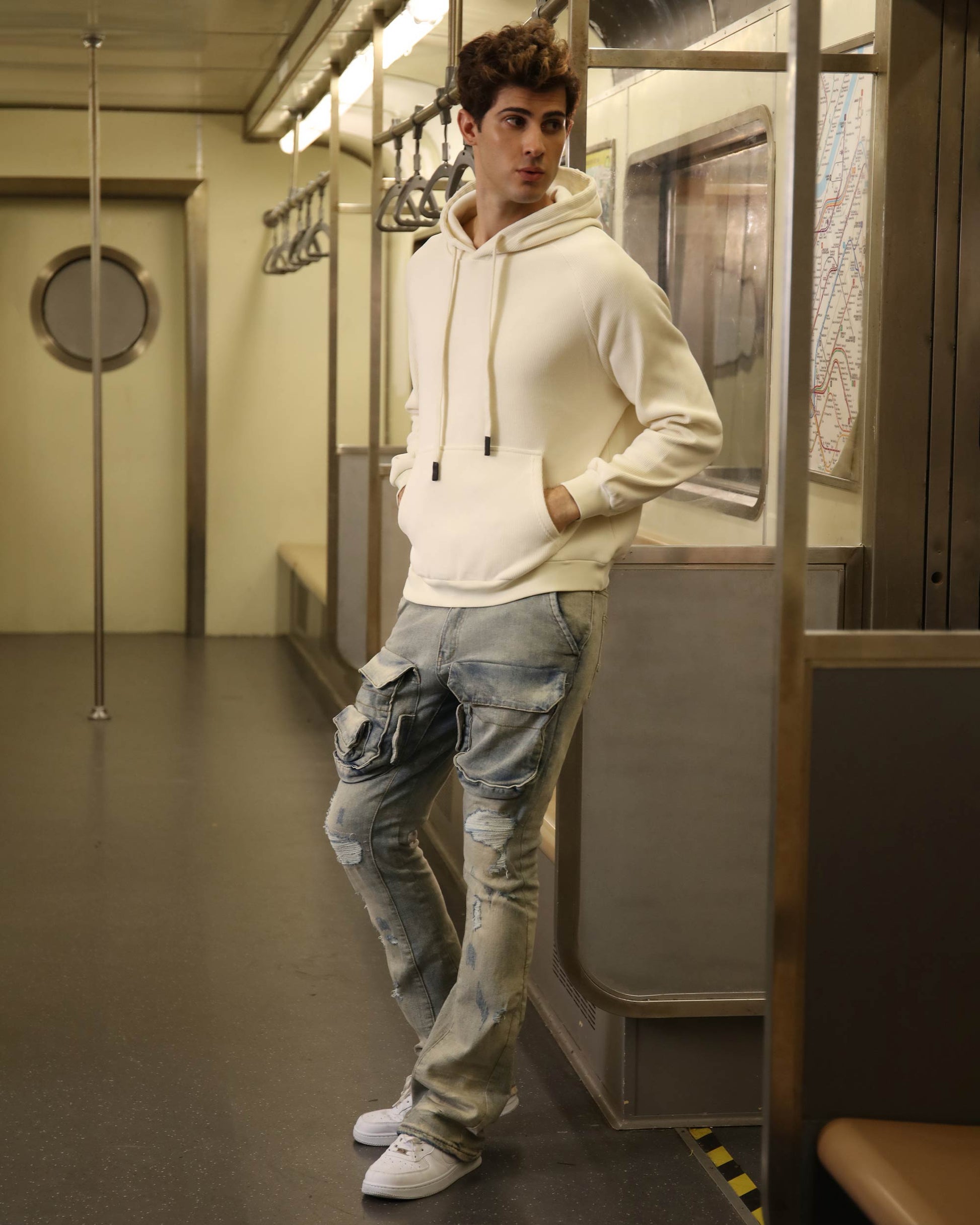 Man wearing light wash cargo jeans and a white hoodie in a subway train setting