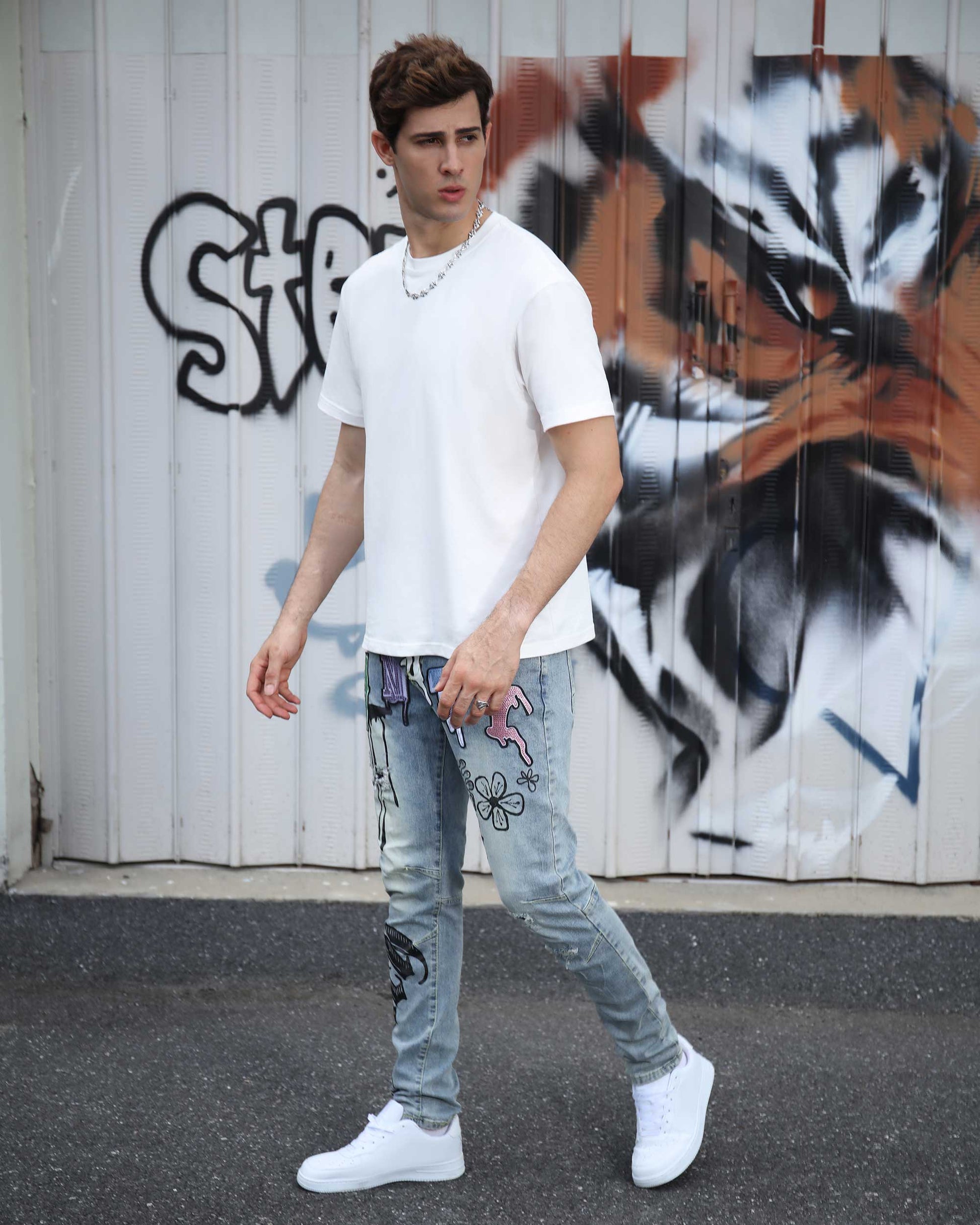 Model wearing Logeqi light wash street art jeans with floral and graffiti designs and white sneakers