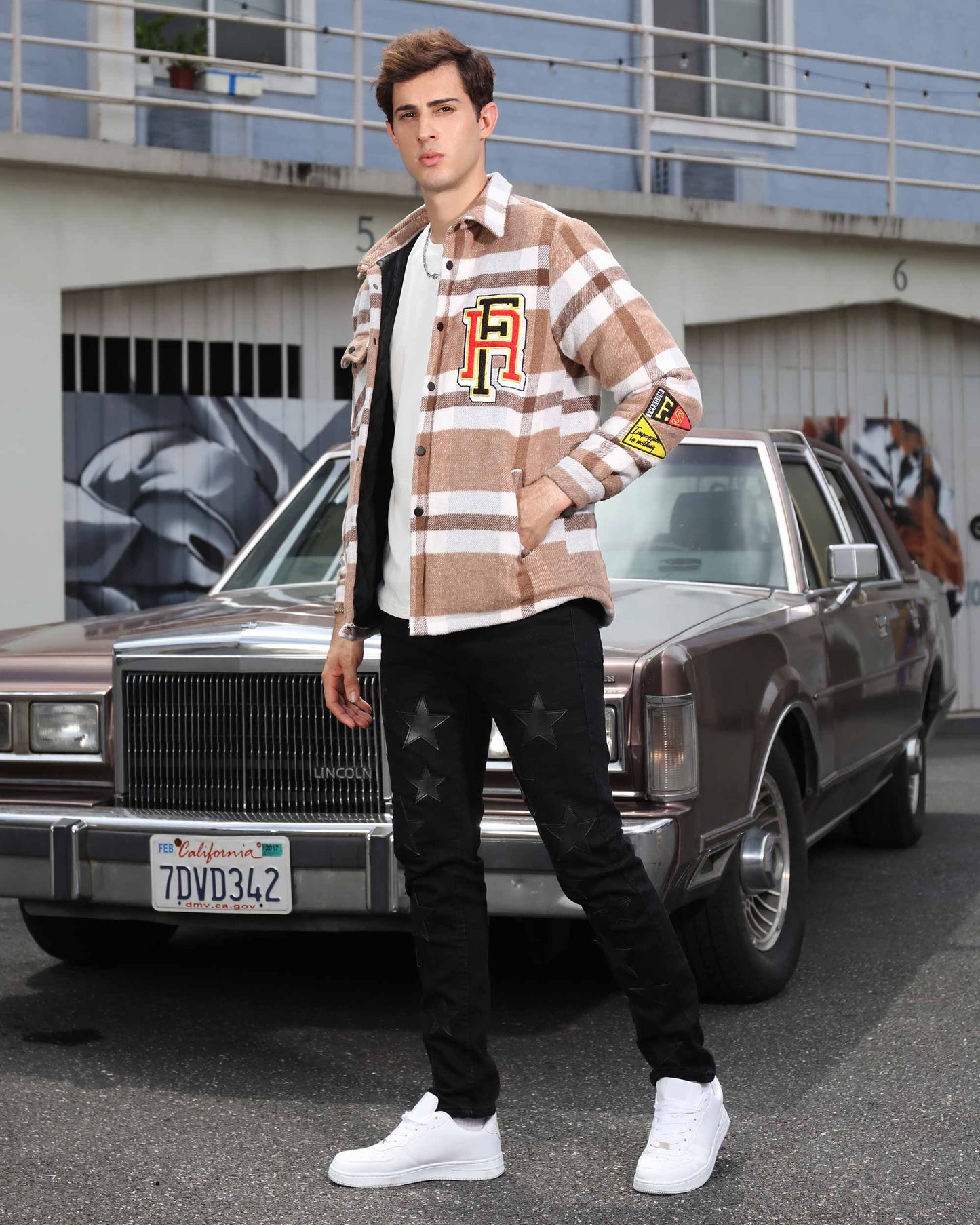 Young man wearing a modern plaid moto jacket by Logeqi with black jeans and white sneakers