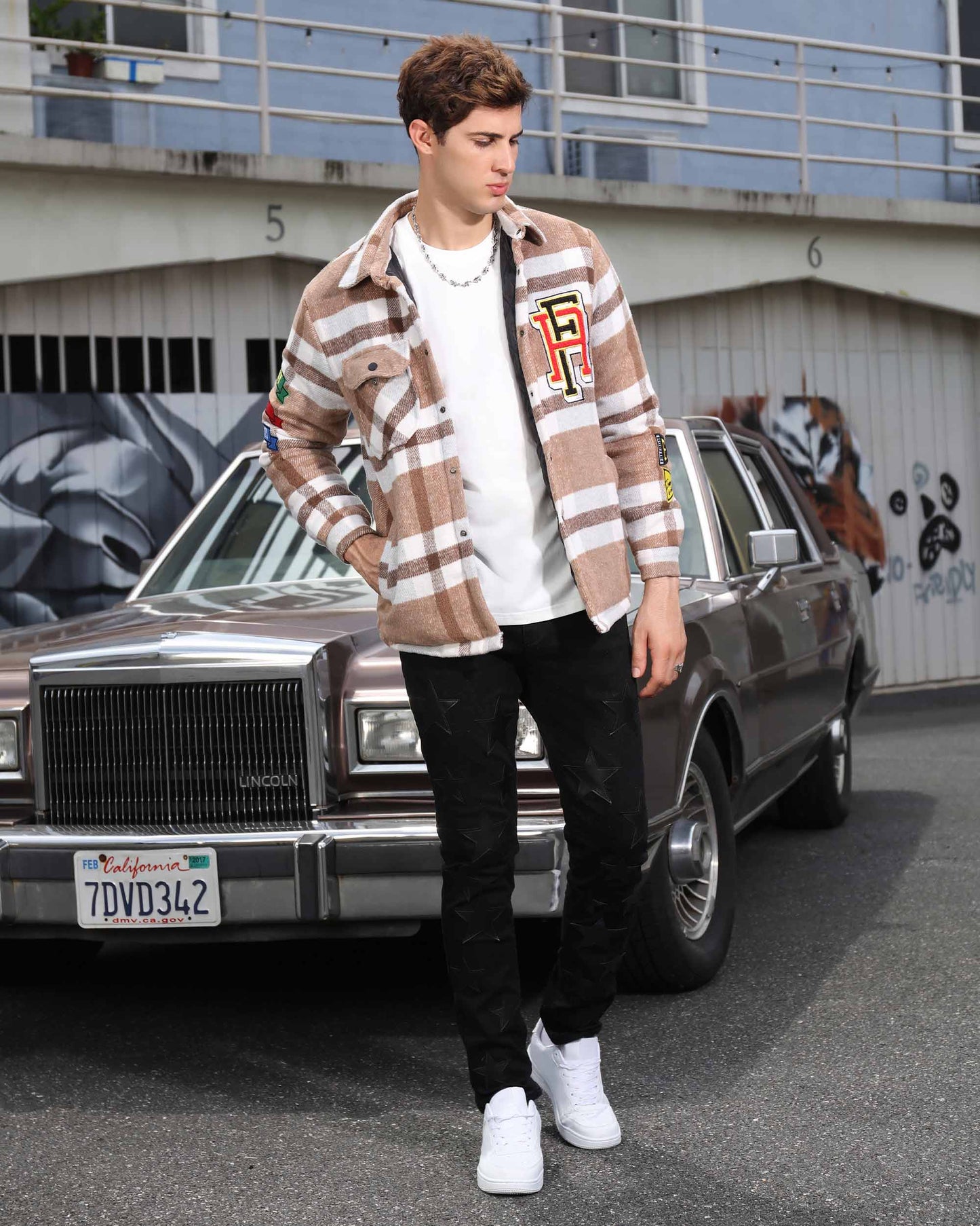 Man wearing Logeqi modern plaid moto jacket in brown white with patches standing in front of vintage car