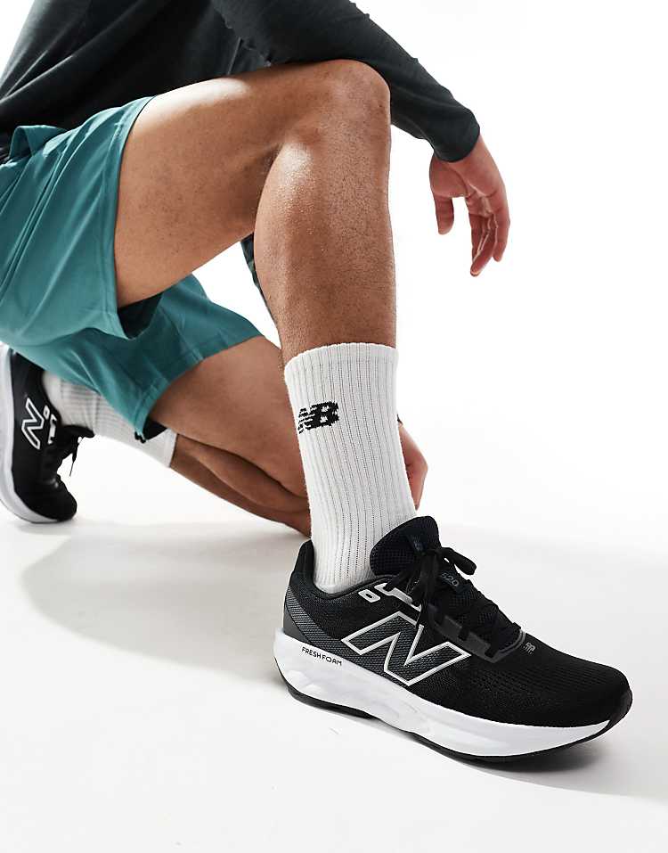 New Balance 520 running shoes in black worn by a man kneeling in blue shorts and white New Balance socks