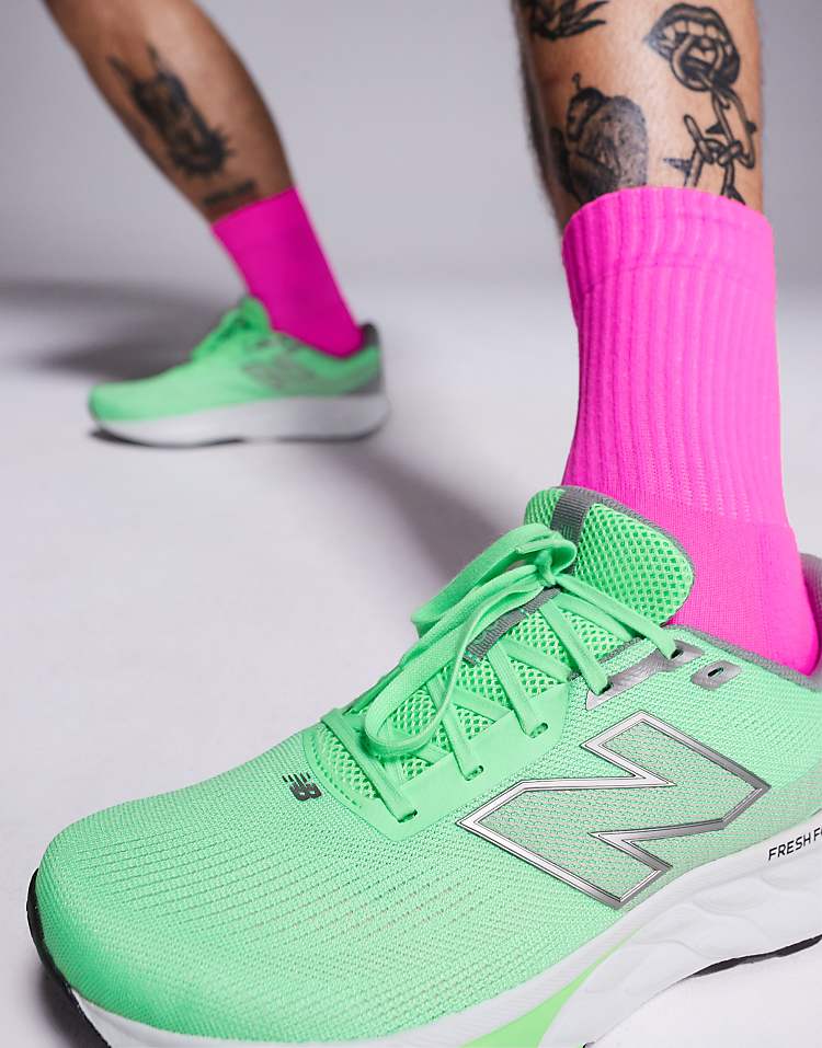 Close-up of neon green New Balance 520 running shoes worn with bright pink socks on tattooed legs