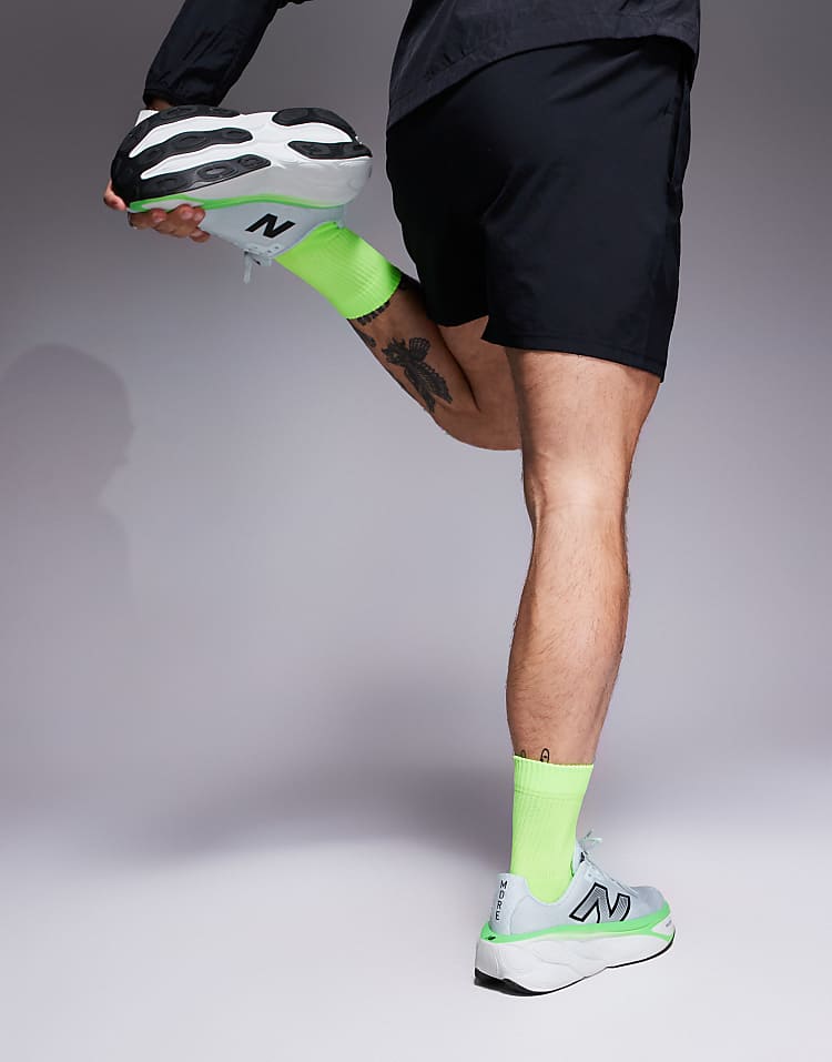 Person wearing New Balance running shoes black with neon green socks and black shorts stretching leg