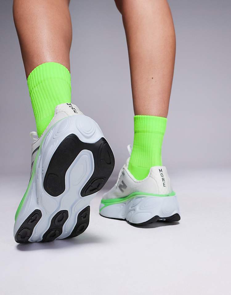 New Balance running shoes in white and green worn with bright green socks on a gray background