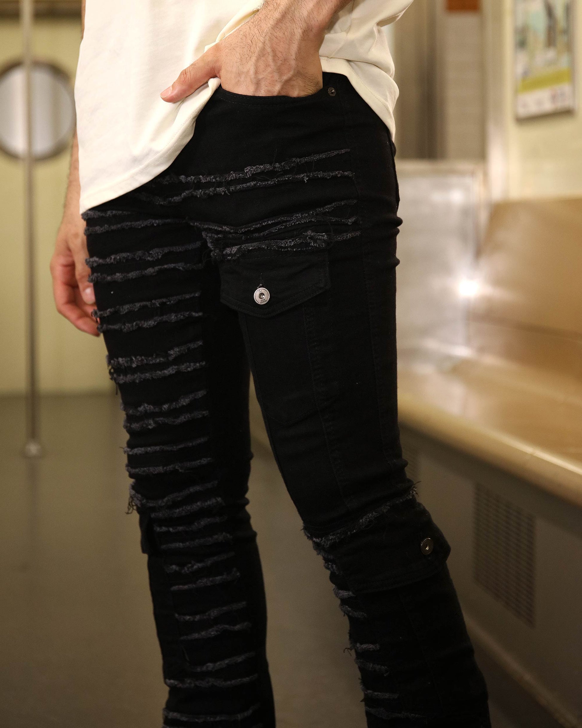 Logeqi raw edge black jeans with ripped detailing and buttoned cargo pockets worn by a man