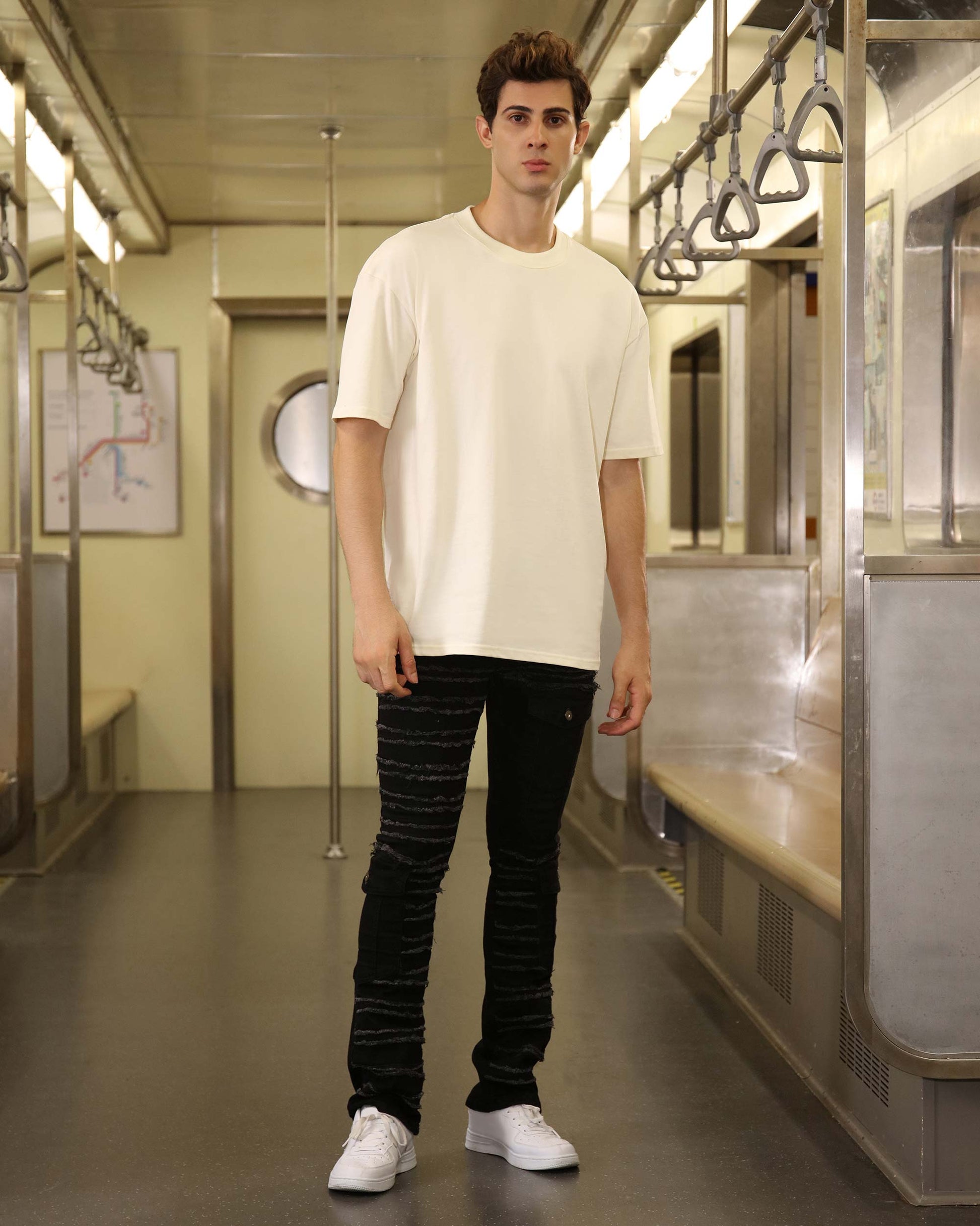 Logeqi raw edge black jeans worn by male model with white shirt and white sneakers in subway