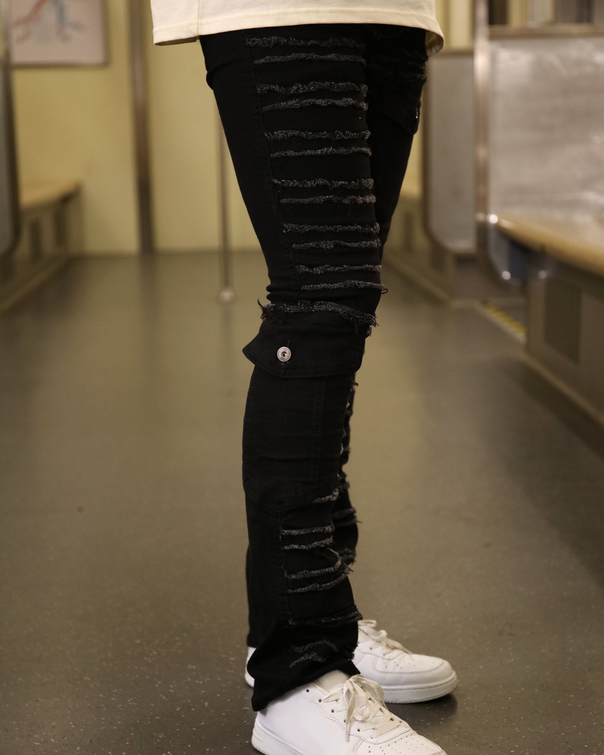 Logeqi raw edge black jeans with distressed details worn with white sneakers on subway floor