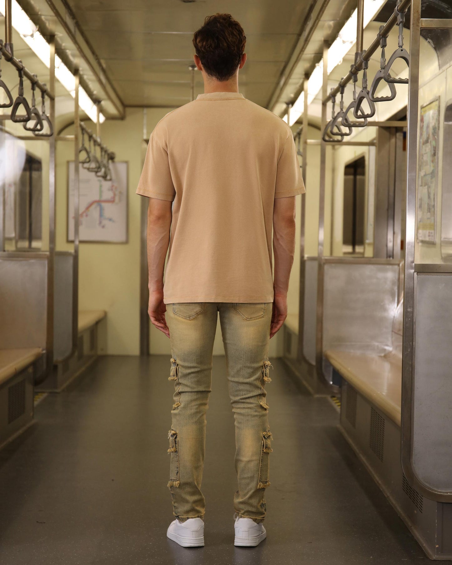 Back view of a man wearing Logeqi raw edge brown jeans with cargo pockets inside a subway train