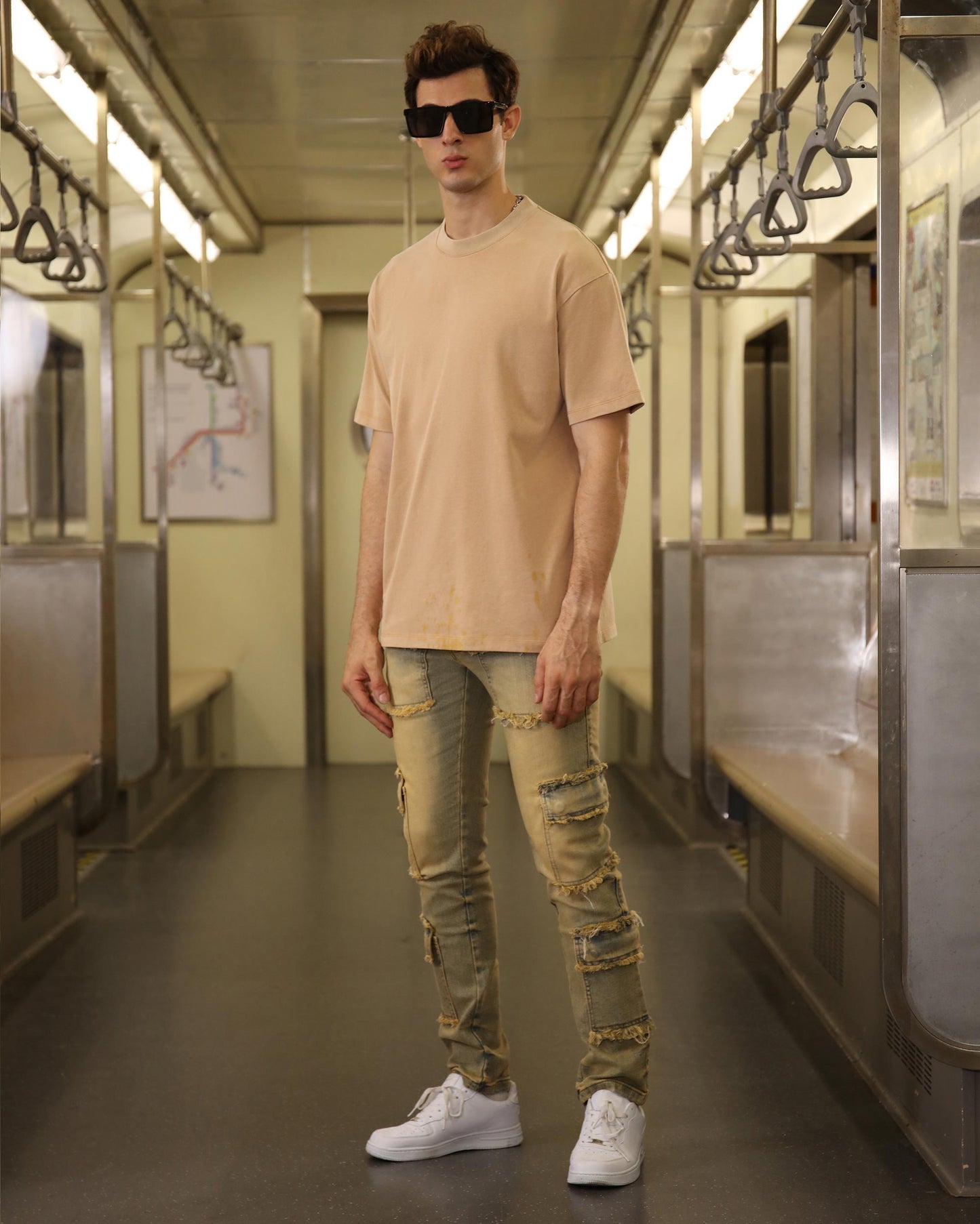 Logeqi raw edge brown jeans with distressed details worn by a male model in a subway train