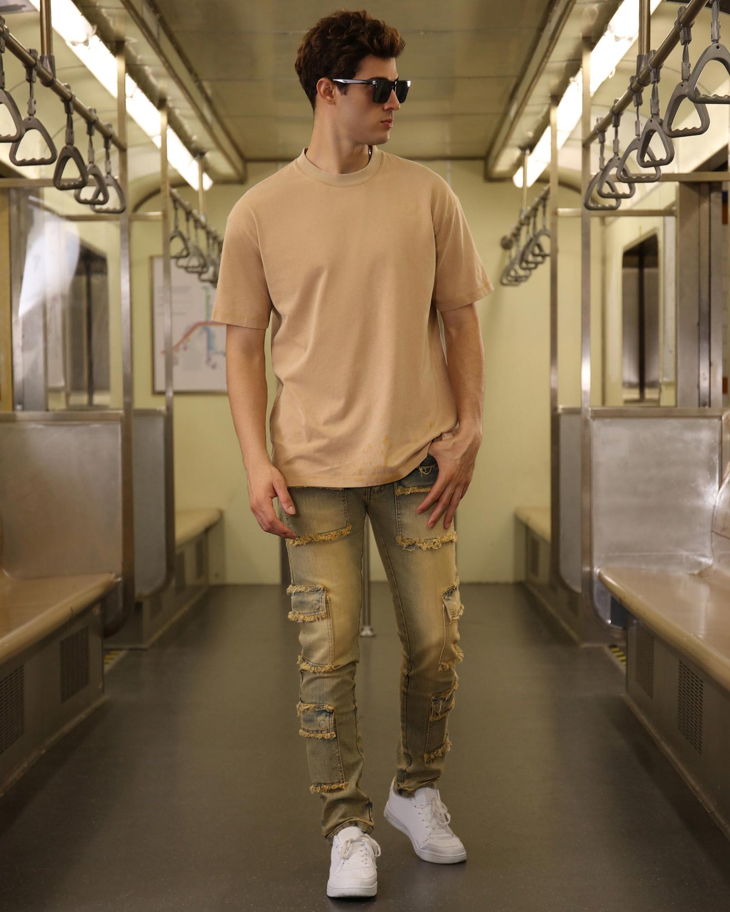 Logeqi raw edge brown jeans with distressed patches worn by a man in a subway setting