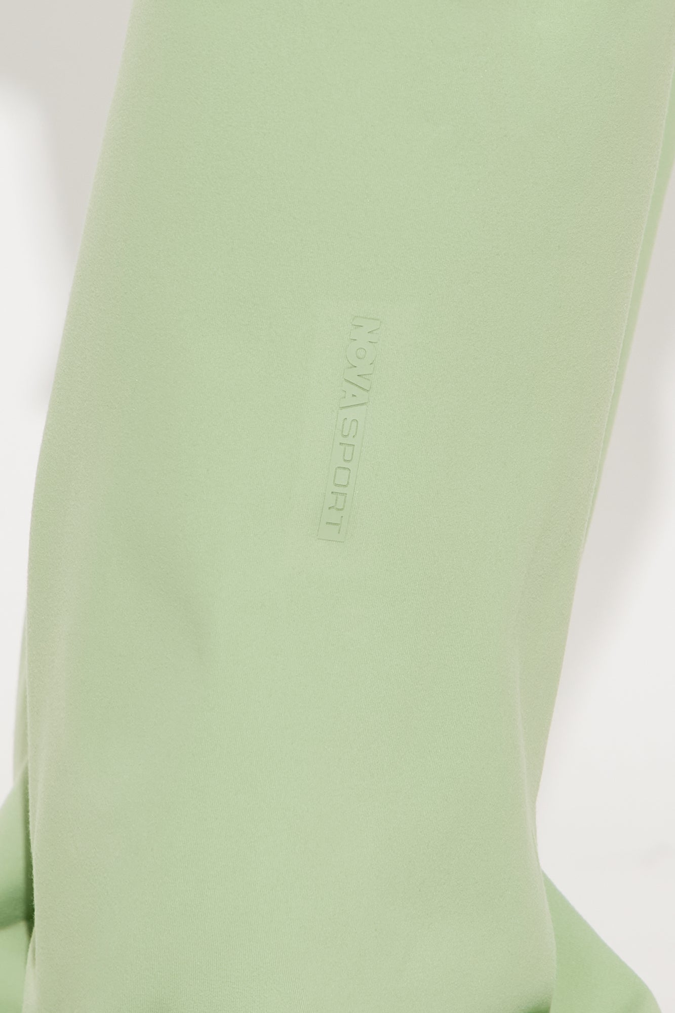 Close-up of Nova Sport logo on sage green active pants for women highlighting the fabric texture