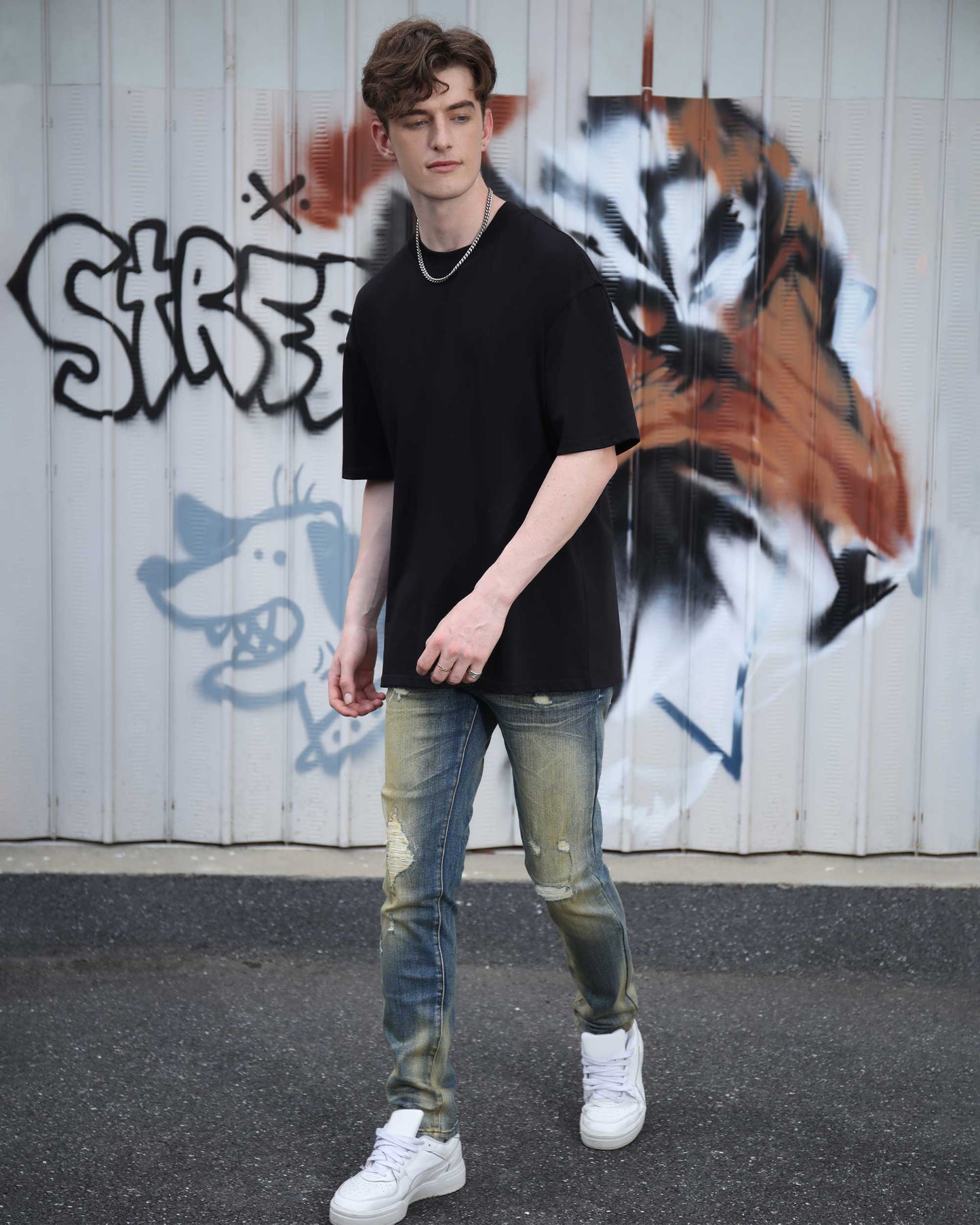 Model wearing Logeqi slim fit blue ripped jeans with a black t-shirt and white sneakers