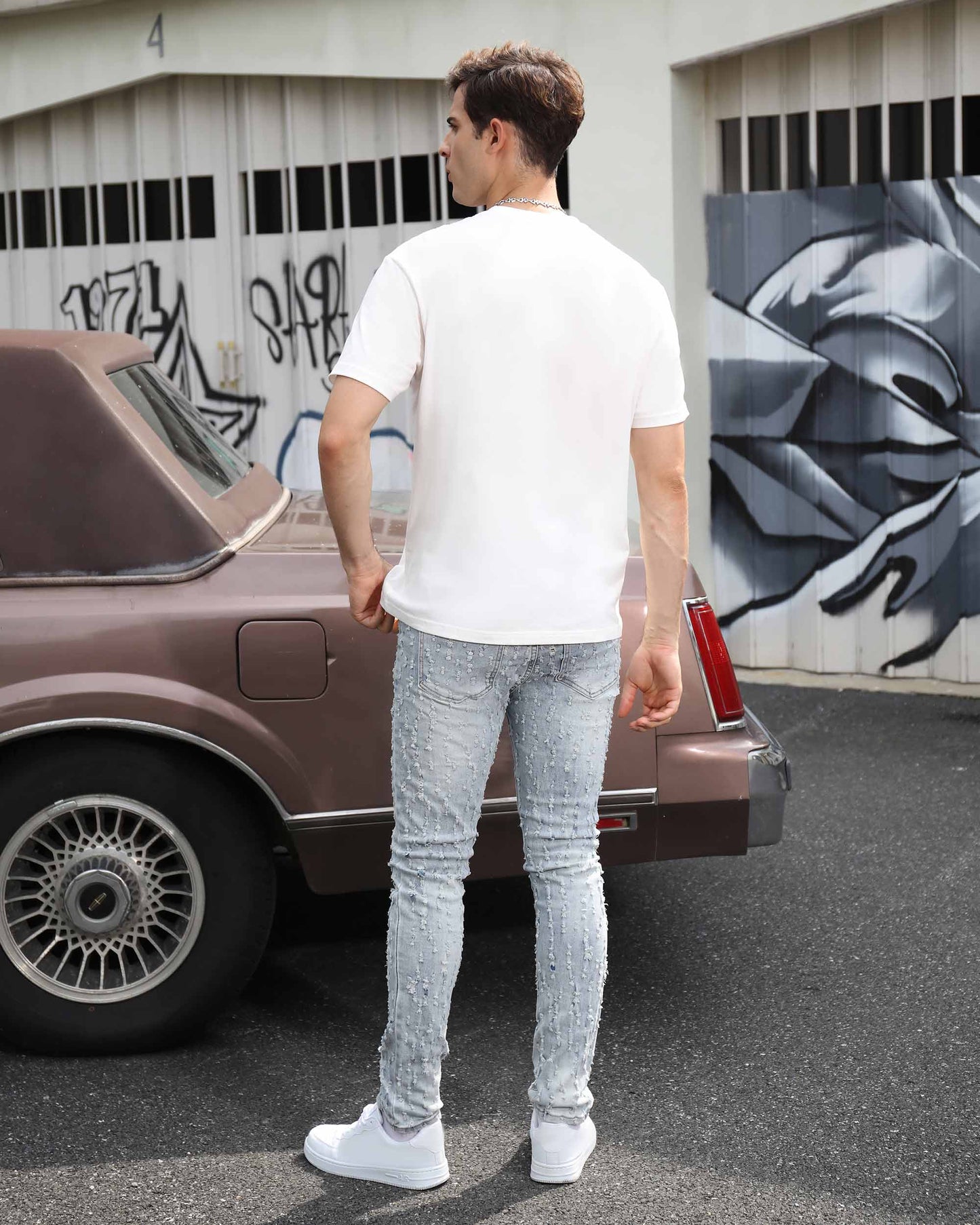 Logeqi slim fit ripped jeans styled on a model standing by a vintage car in a street art setting